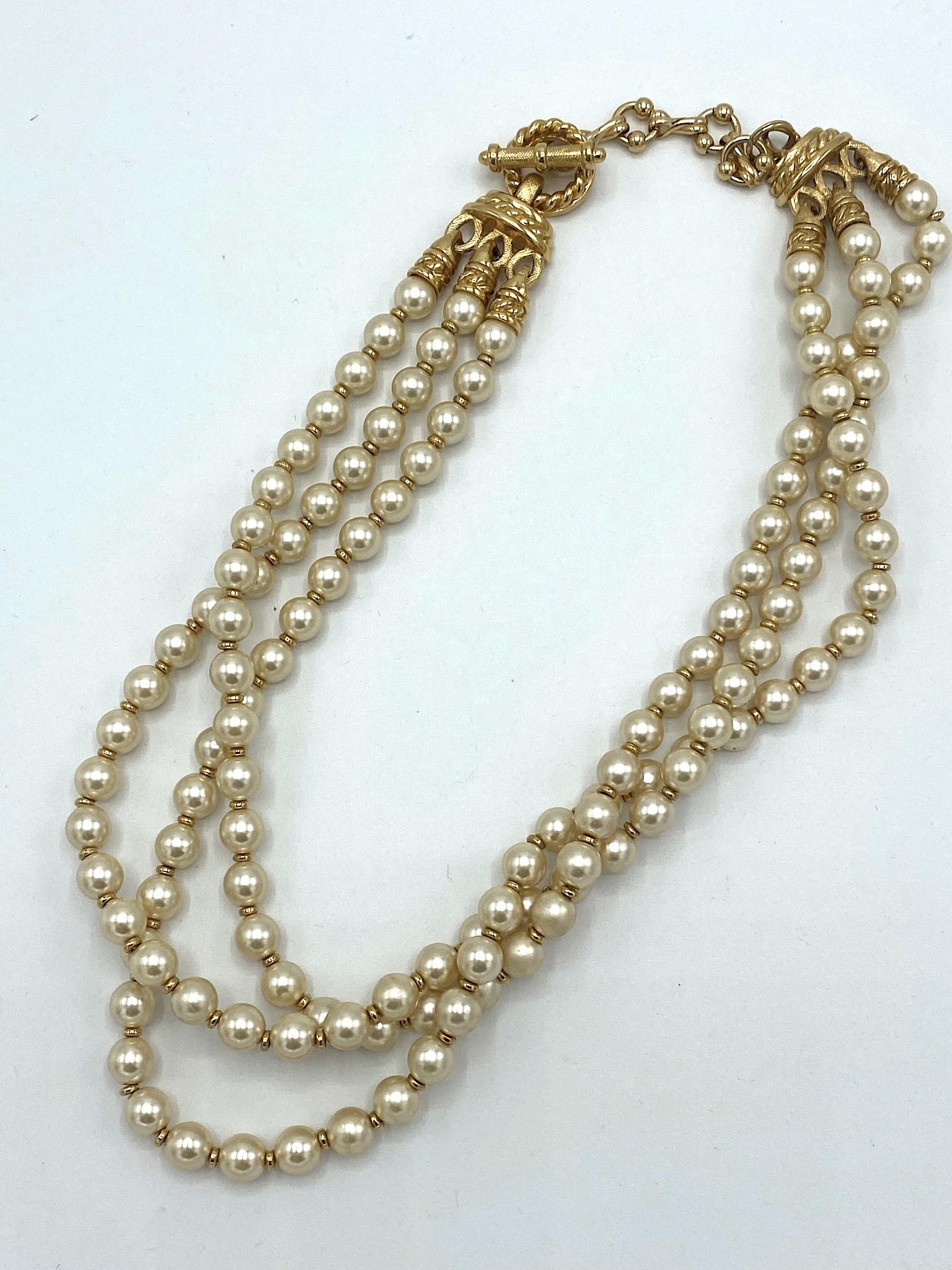 Classic three stand necklace by American fashion house St. John. Three strands of creamy white 8 mm faux pearls are strung with small gold disk spacer beads. The end beads are finished with gold rope twist design end caps and attach to the multi