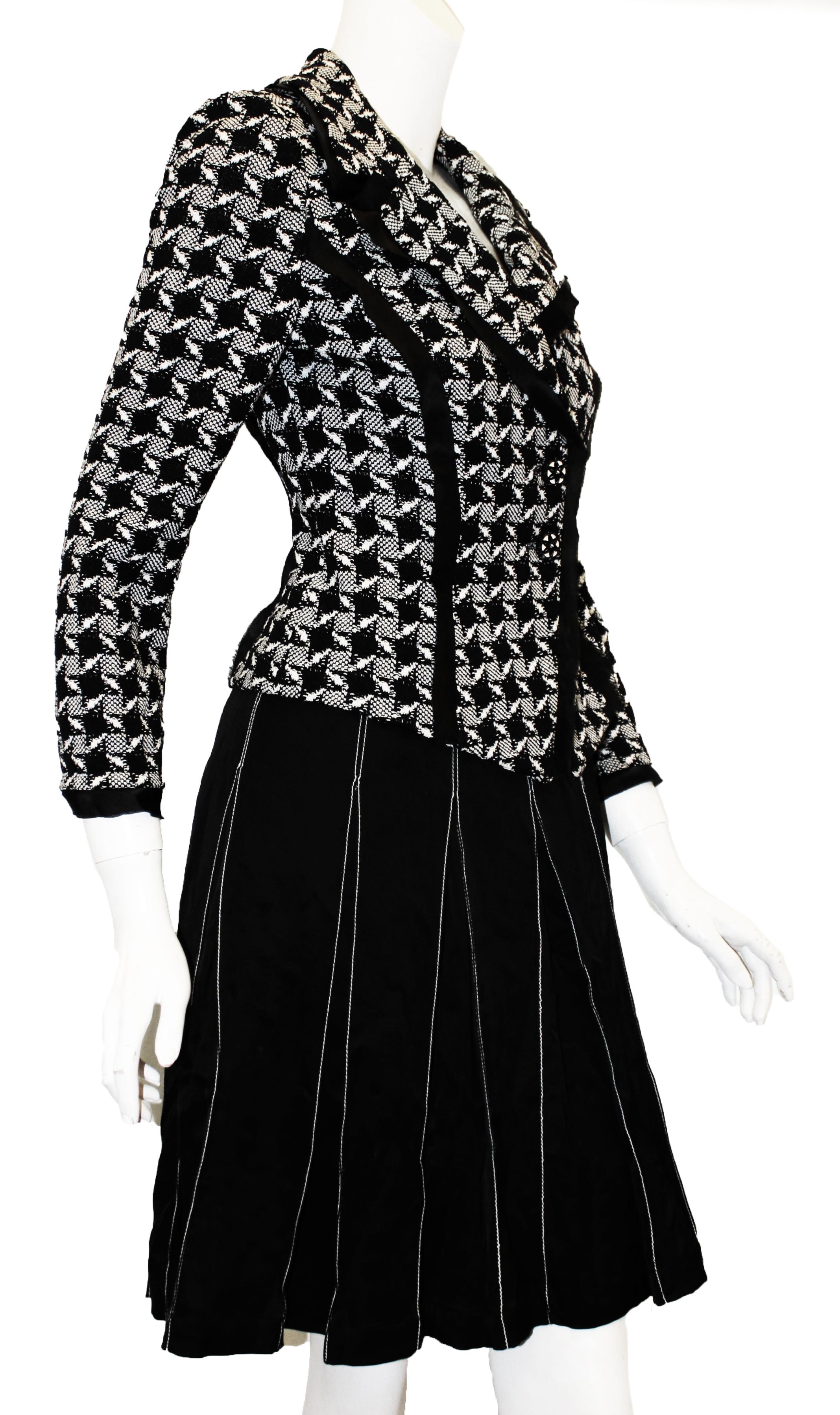 St. John black and white pleated skirt suit is lined in black silk.  The skirt includes top stitching in contrasting white thread from waist to hem.  The knit jacket's design is checkerboard allover and is trimmed with frayed black silk around the