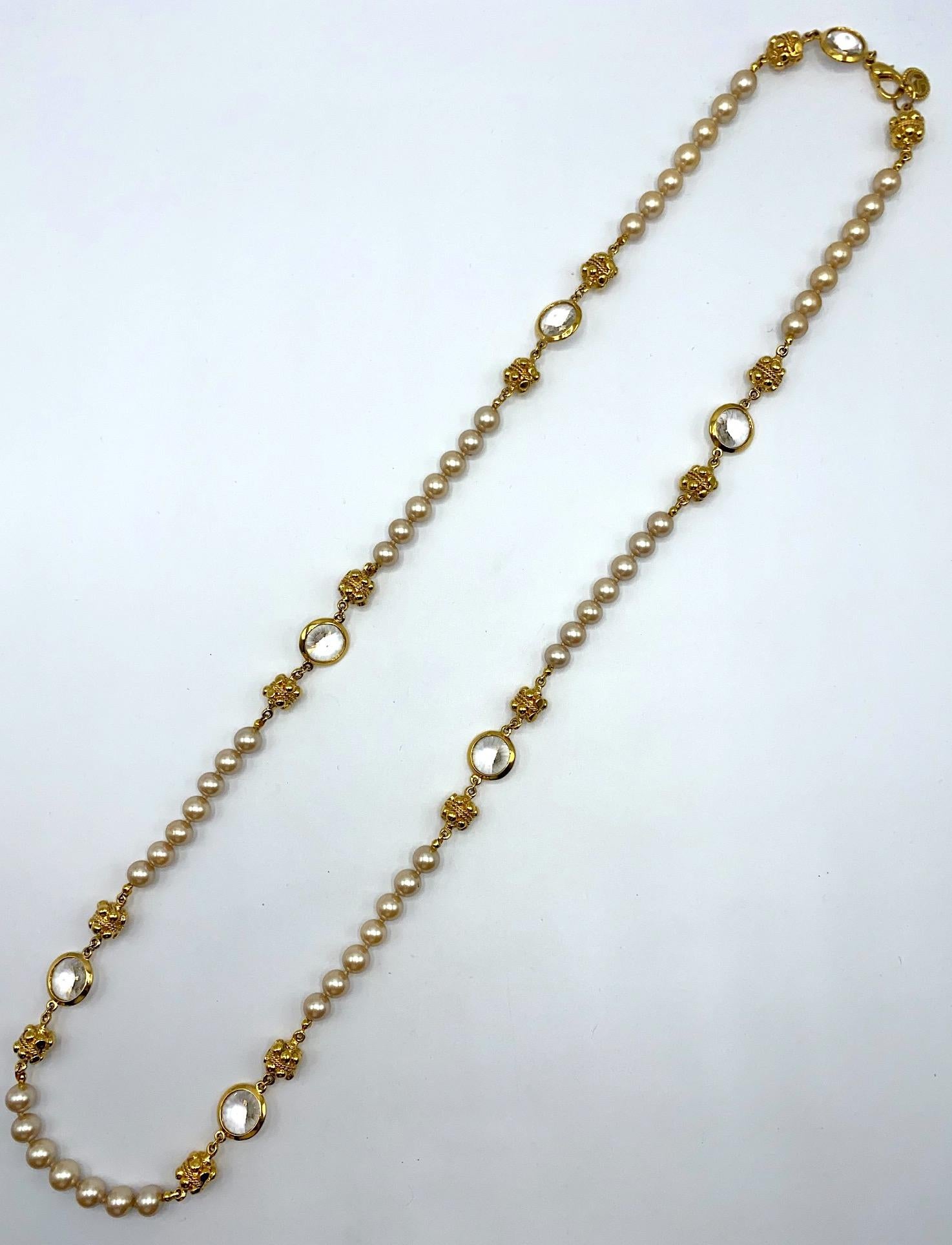 A very finely made and elegant St. John Collection long necklace in gold plate, faux pearls and crystals from the 1990s. Each 10 mm size glass center faux pearl is individually knotted in strands of 7 pearls that alternate with two fancy cast gold 