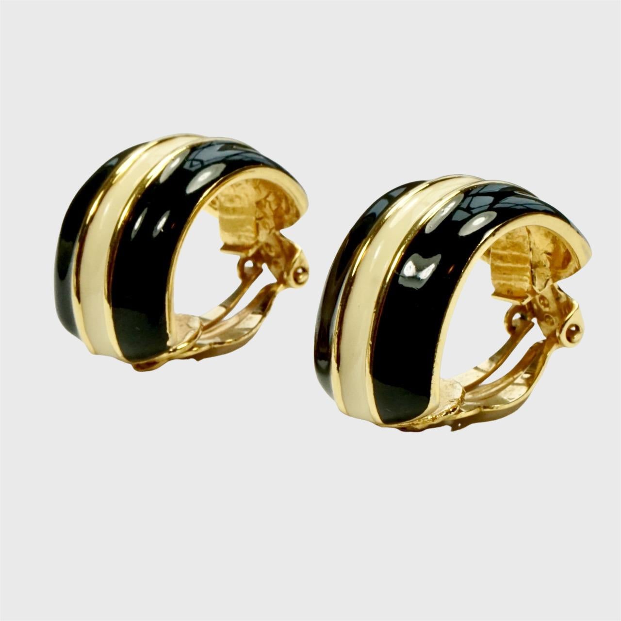 Graziosi orecchini a clip a mezzo cerchio placcati oro con smalto nero e crema. Misura 2,2 cm di lunghezza e 1,65 cm di larghezza.

Si tratta di un paio di orecchini dal design classico, risalenti agli anni '80 circa.