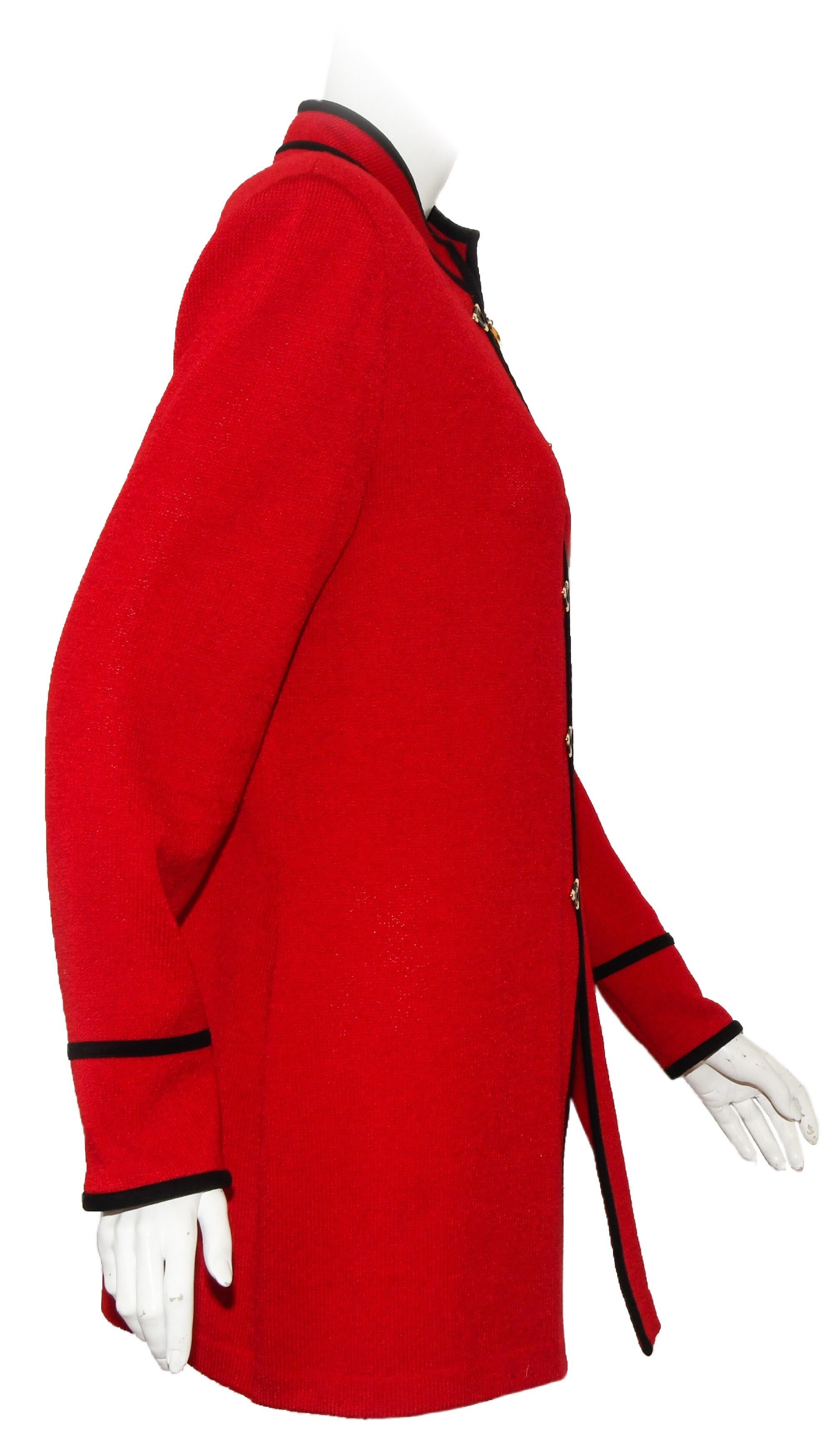 St. John red long knit jacket incorporates an up collar and it's trimmed with black knit around collar and down the front and double trim around cuffs.  This jacket has a zipper at front for closure and is decorated with faux black and gold tone