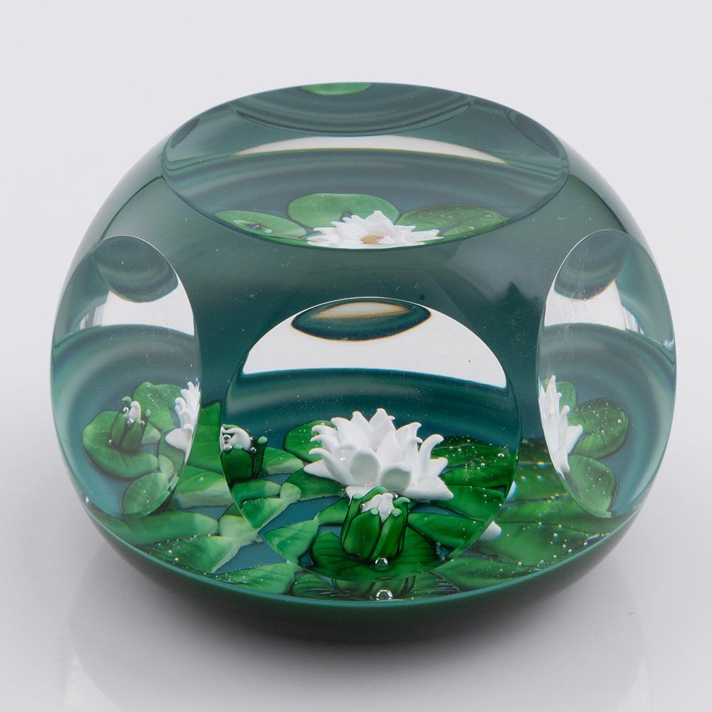 Heading : St Louis Paperweight Lampwork Millefiori Lily Pond 1981
Date : 1981
Origin : France
Features :  Lampwork and millefiori lily flower and two buds  and green leaves floating on a turquoise base. Six facet cut side  windows and a top