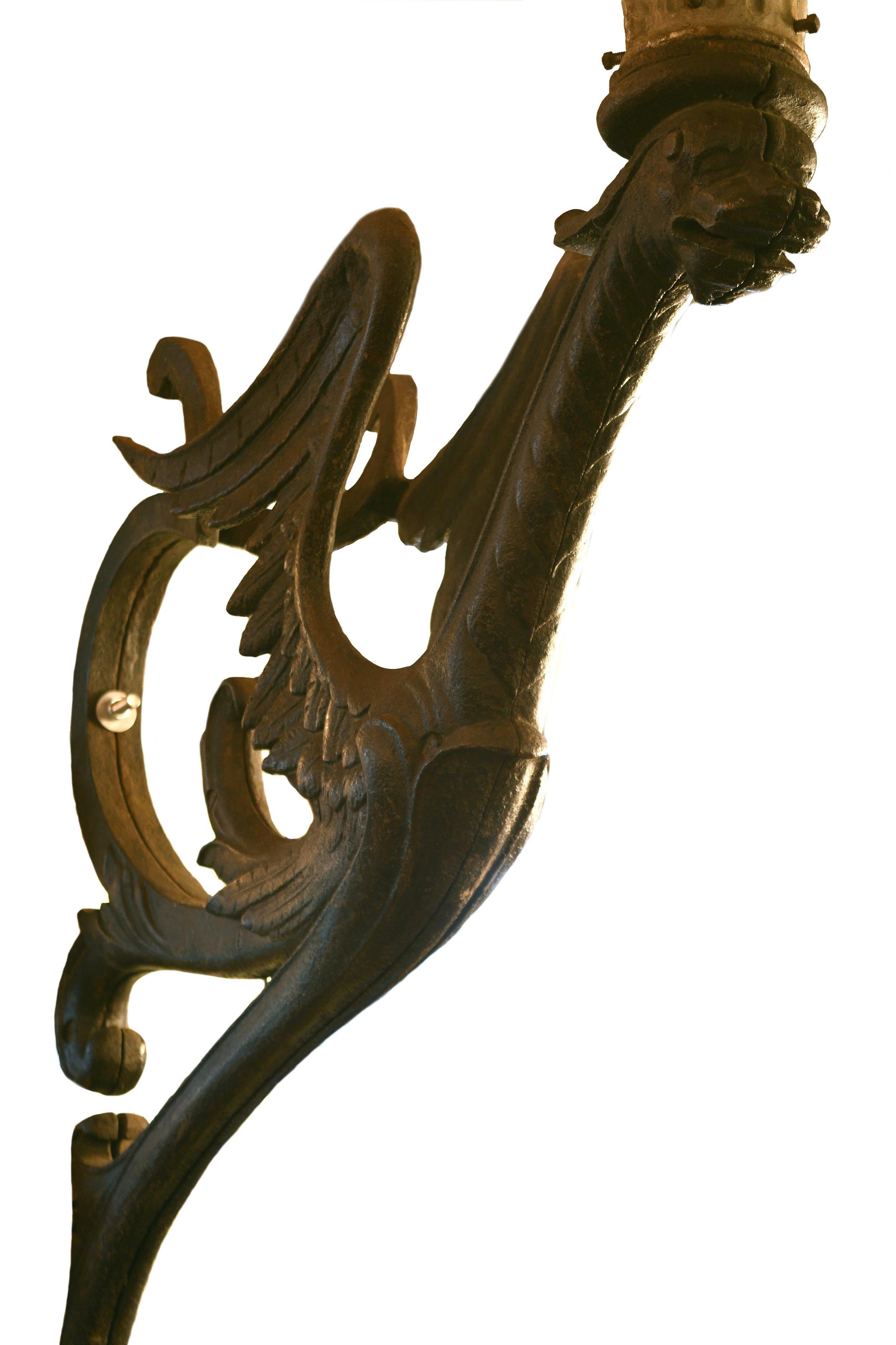 This massive cast iron winged dragon sconce was once used to illuminate the St. Louis World's Fair of 1904. An oversized and luminous cylindrical lamp rests above the dragon’s head. The dragon’s body features intricately detailed wings and a long