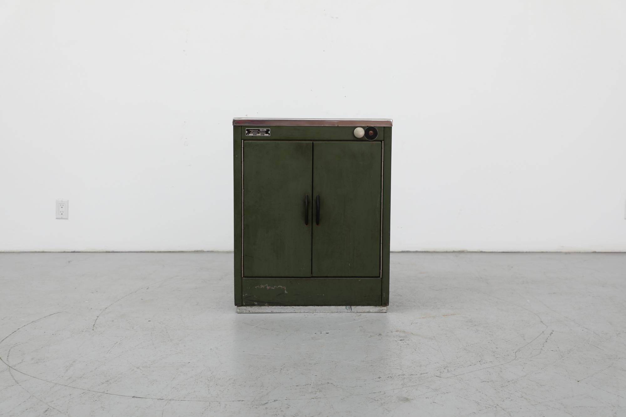 Belgian dark green enameled metal utility cabinet with bake-lite handles and teak shelf added. In otherwise original condition with visible wear, including scratches. Great little entry cabinet. Wear is consistent with its age and use.