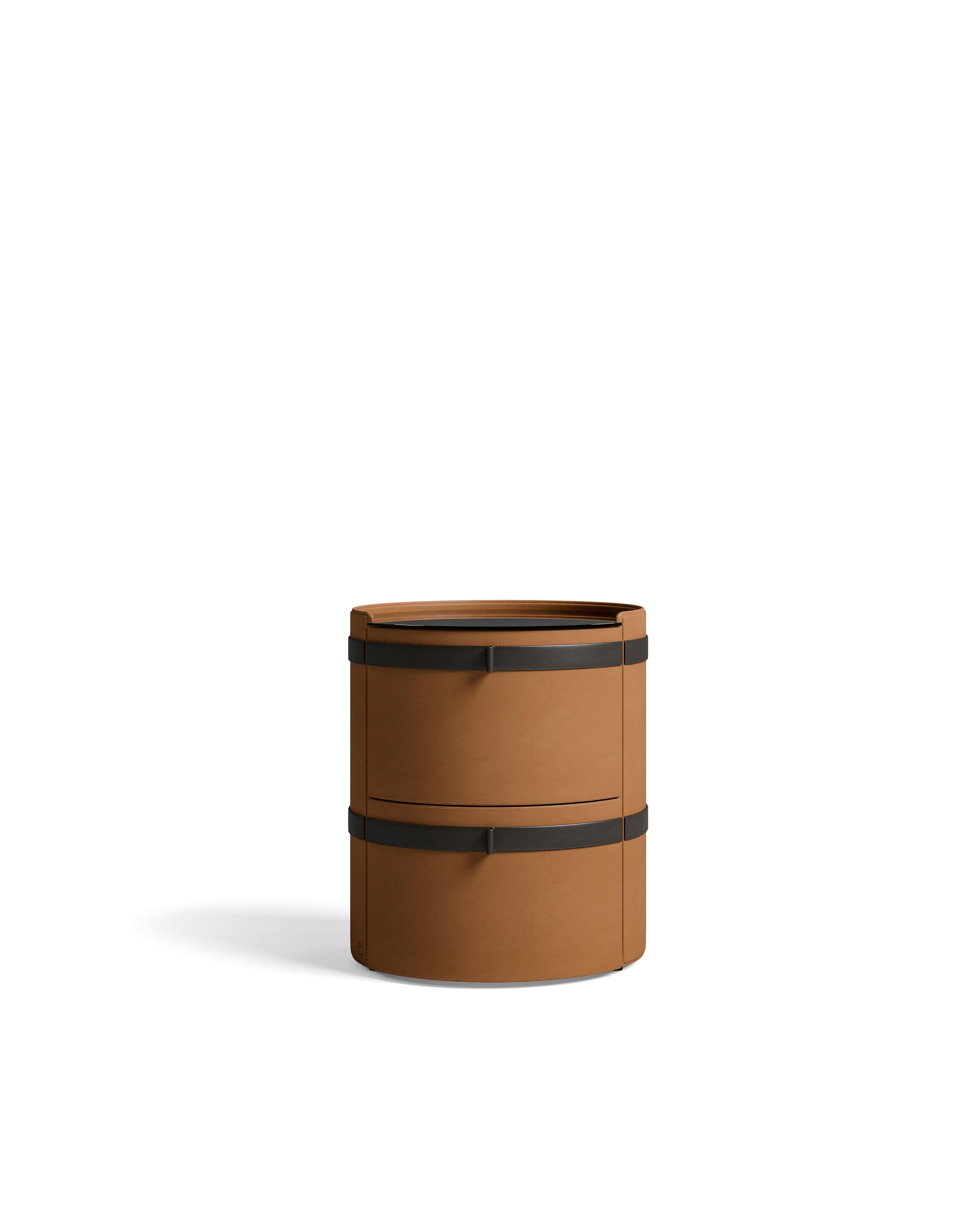 A round bedside table entirely covered in saddle leather with a smoked glass top. The table features a sleek, modern design with a soft yet durable saddle leather finish, providing both elegance and functionality. The smoked glass top adds a