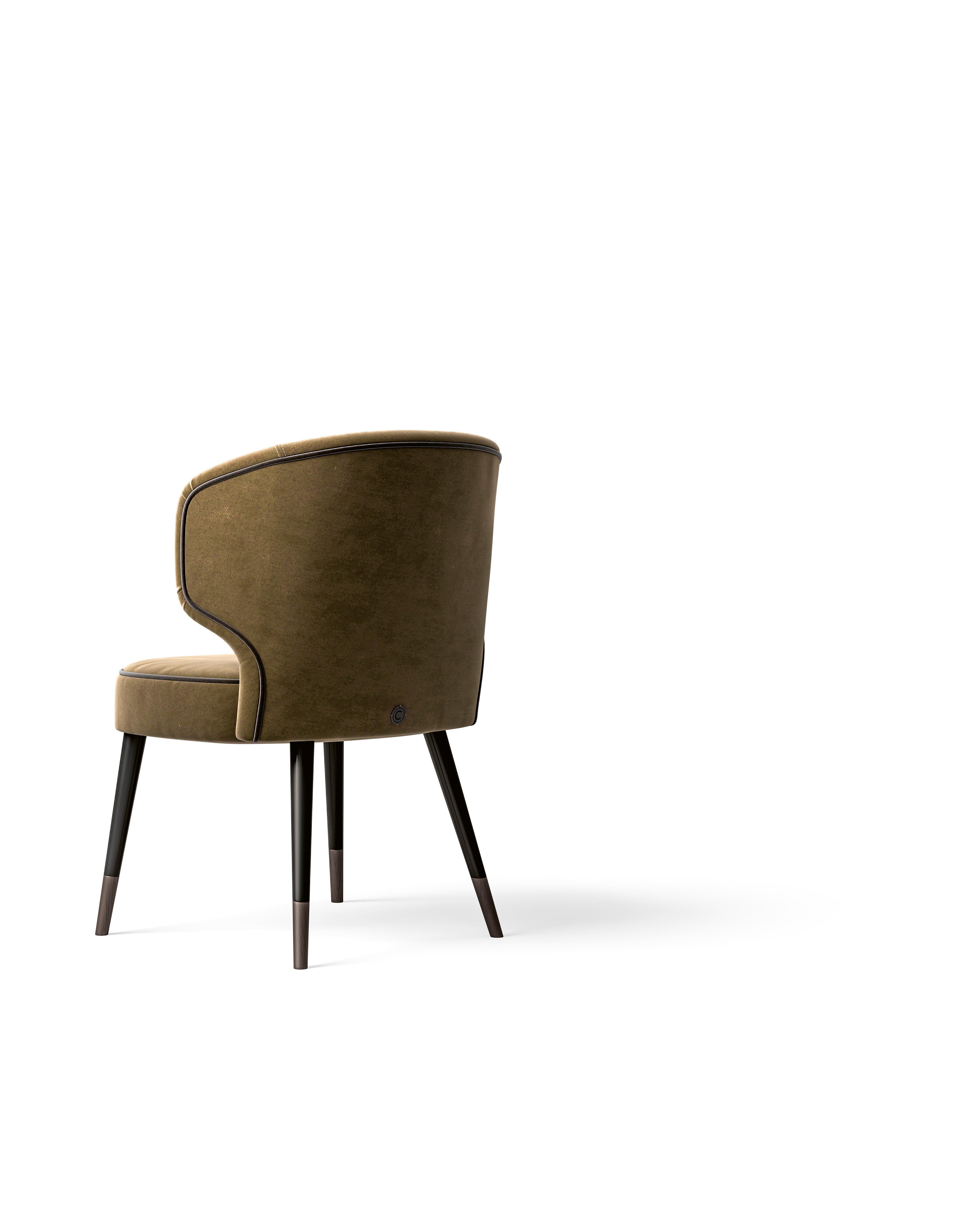 Una silla que puede tapizarse en piel o tela, con ribetes en contraste para darle un toque de estilo. Las patas son de metal, lo que añade un toque elegante y moderno al diseño. Esta silla versátil combina elegancia y comodidad, y ofrece una