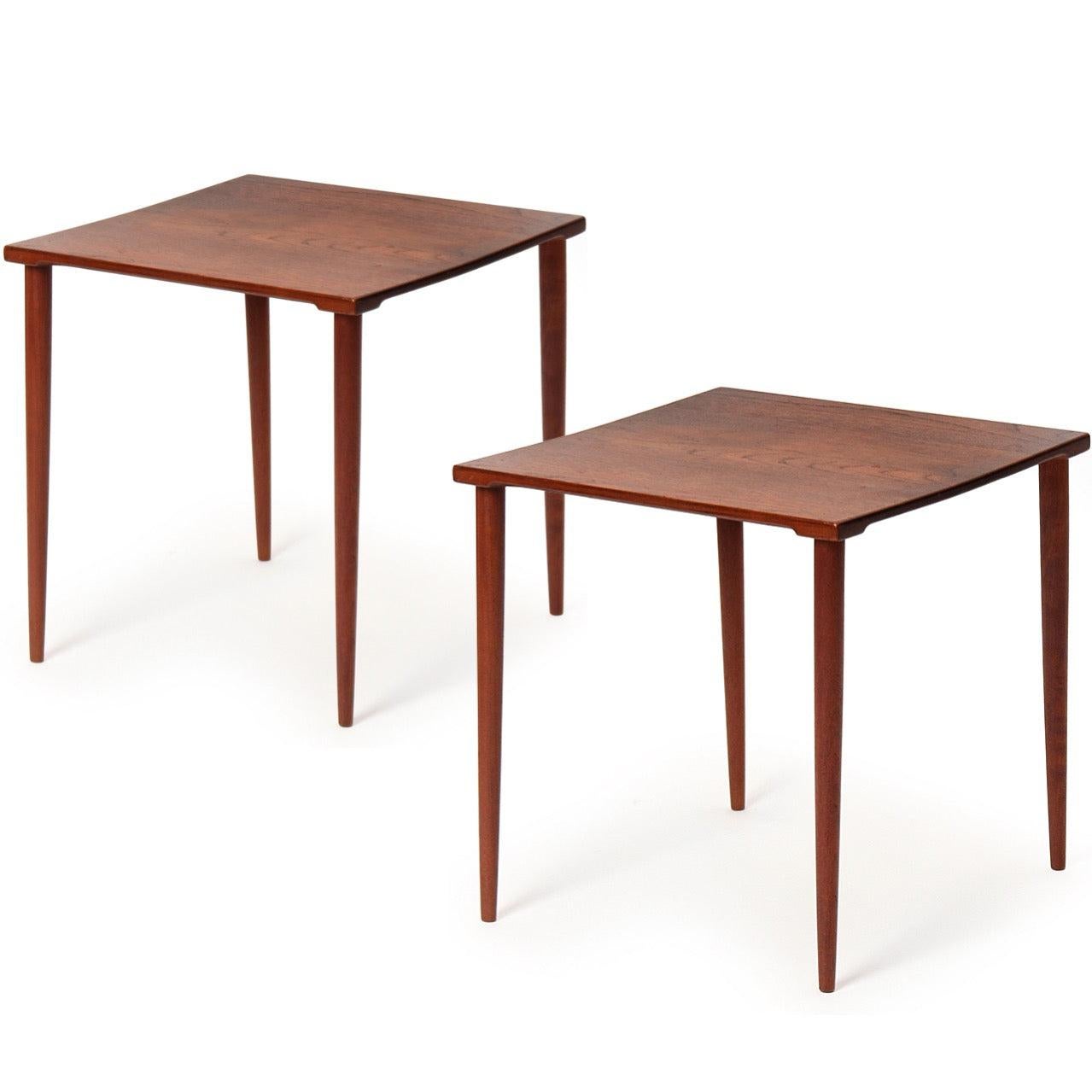 A stackable solid teak end table with shaped edges on turned teak legs with brass connections.