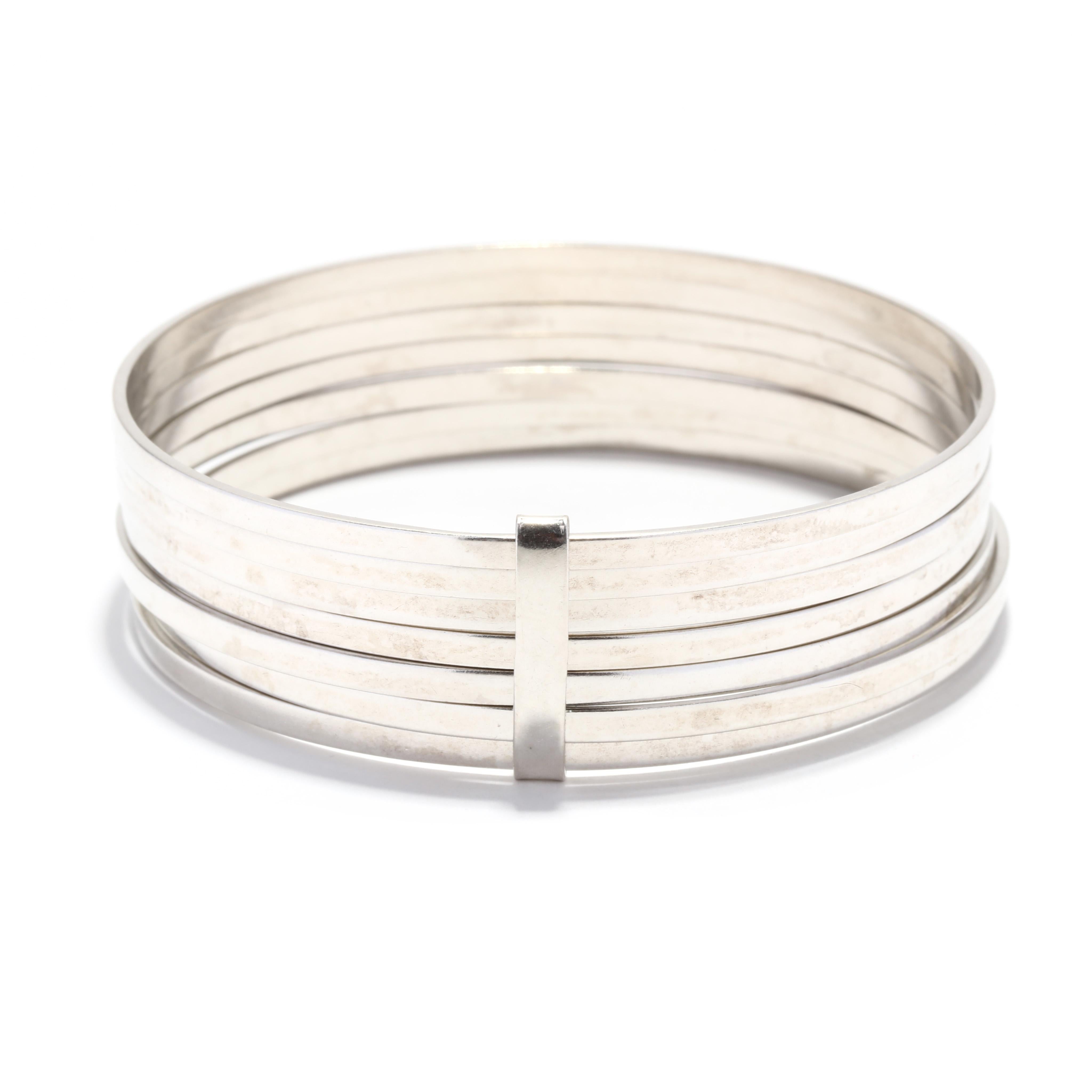 Un ensemble de bracelets empilés en argent sterling. Ce large bracelet est composé de sept bracelets en argent, reliés par une barre d'espacement. Il est estampillé 925.

Largeur : 3/4 in.

Circonférence intérieure : 8.5 pouces

Poids : 36,5 dwt. /