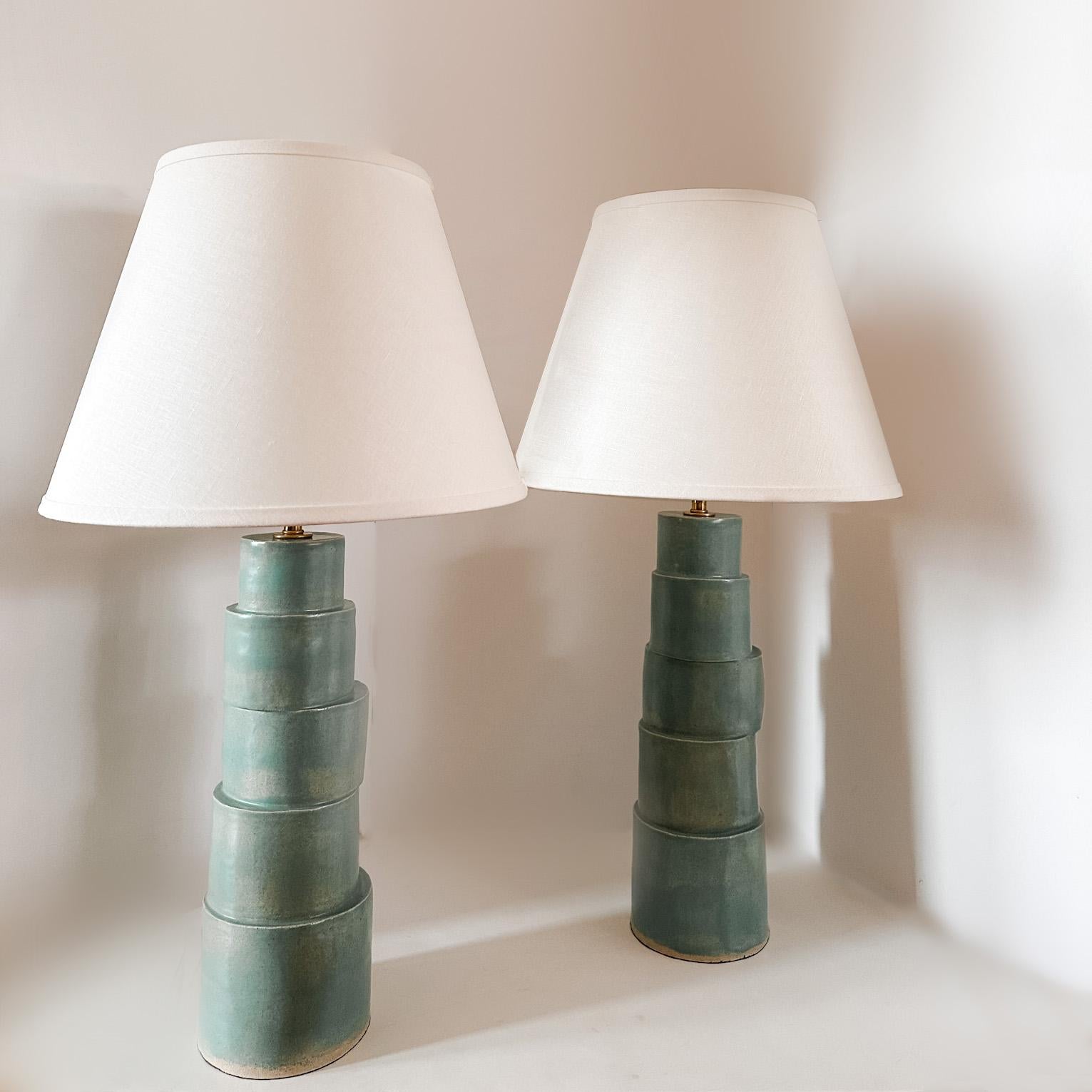 The Stacked column table lamp is handmade in raku clay in a turquoise glaze with brass components, silver fabric cord, and an ivory linen shade. The repetitive nature and asymmetrical design will bring interest to any modern or transitional home.