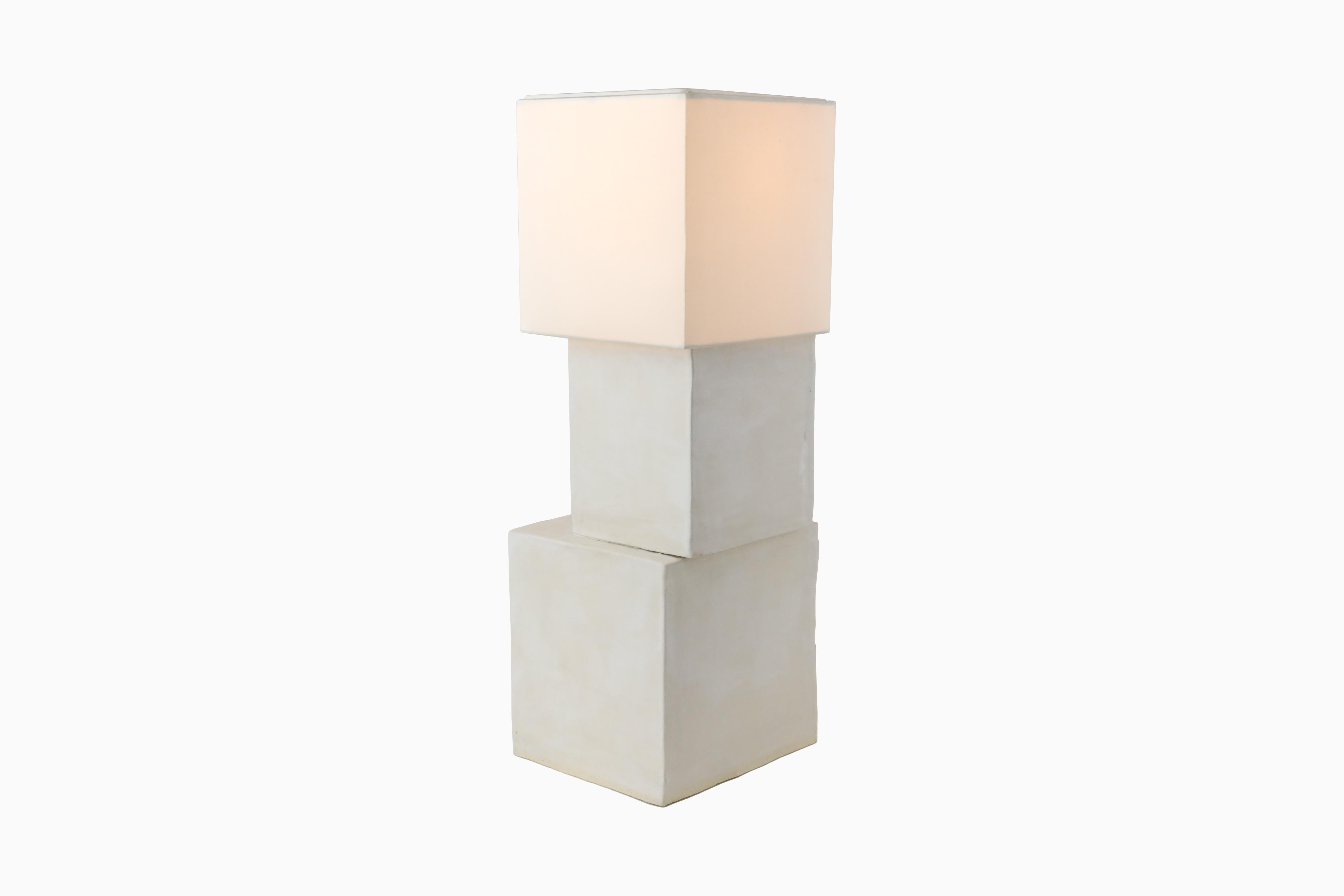 La lampe Stacked Cube a été inspirée par l'architecture moderne de la ville de New York. Chaque cube est fabriqué en argile blanche et recouvert d'une glaçure blanche mate. Les cubes sont assemblés de manière décentrée mais trouvent un équilibre