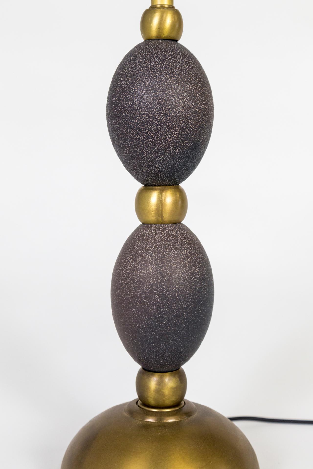 A contemporary lamp fashioned with large, brass beads between two stacked, naturally speckled, emu eggs and a half-sphere, brass base. Wired with a dimmer on the switch; black, fabric covered cord. Measures: 22