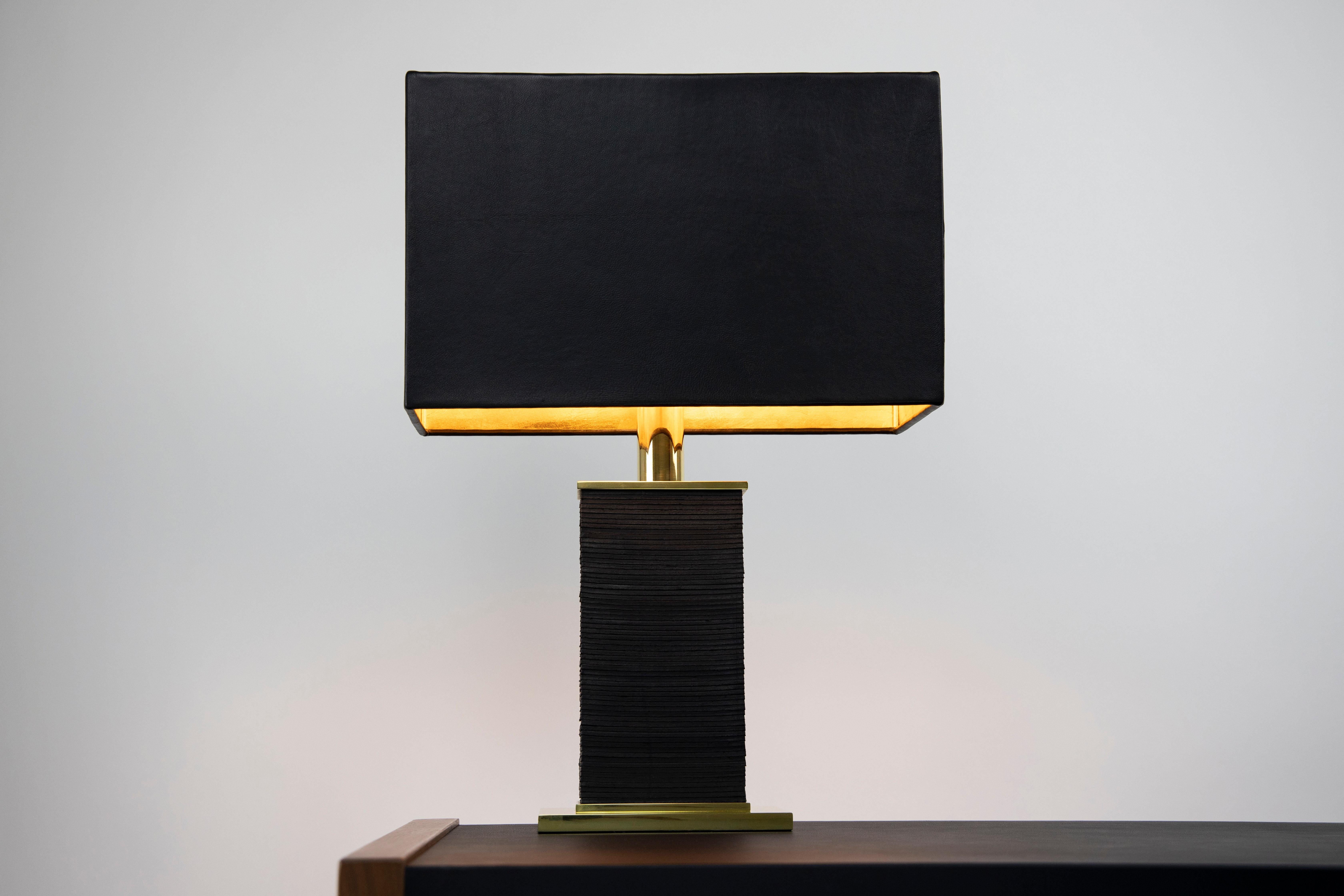 The stacked monolith table lamp is grounded, powerful, and sexy. Its silhouette is modern and simple, yet detailed and tactile up close. The body is made of stacked polished and waxed solid brass plates and saddle leather. Please note that the brass
