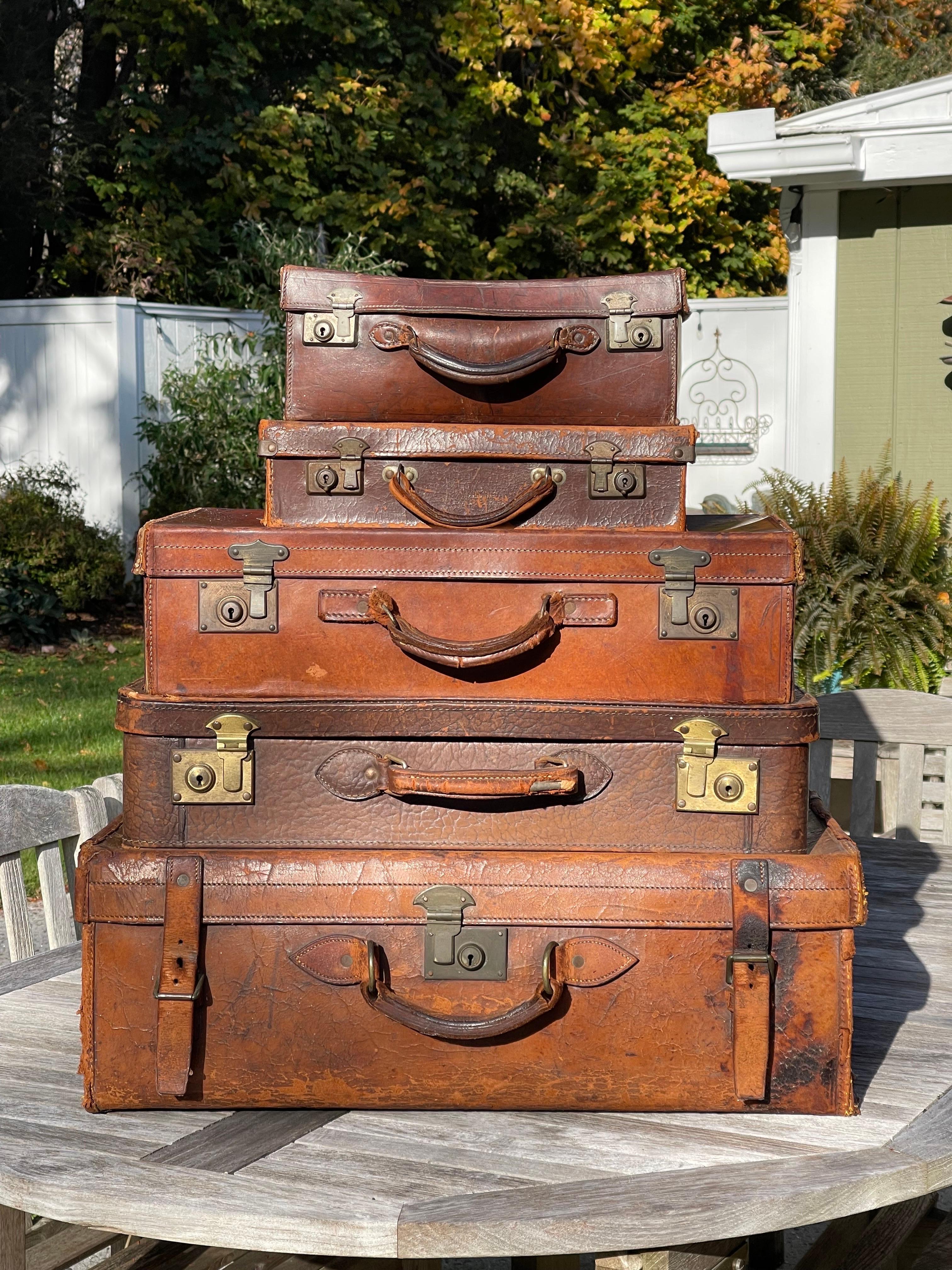 Stacked Set of 5 Antique Leather Suitcases or Trunks. If these suitcases could talk. The stories they would tell. Well worn and loved these leather suitcases have rich patina and history. 
Use as a decorative accent in a guest room or use as a side
