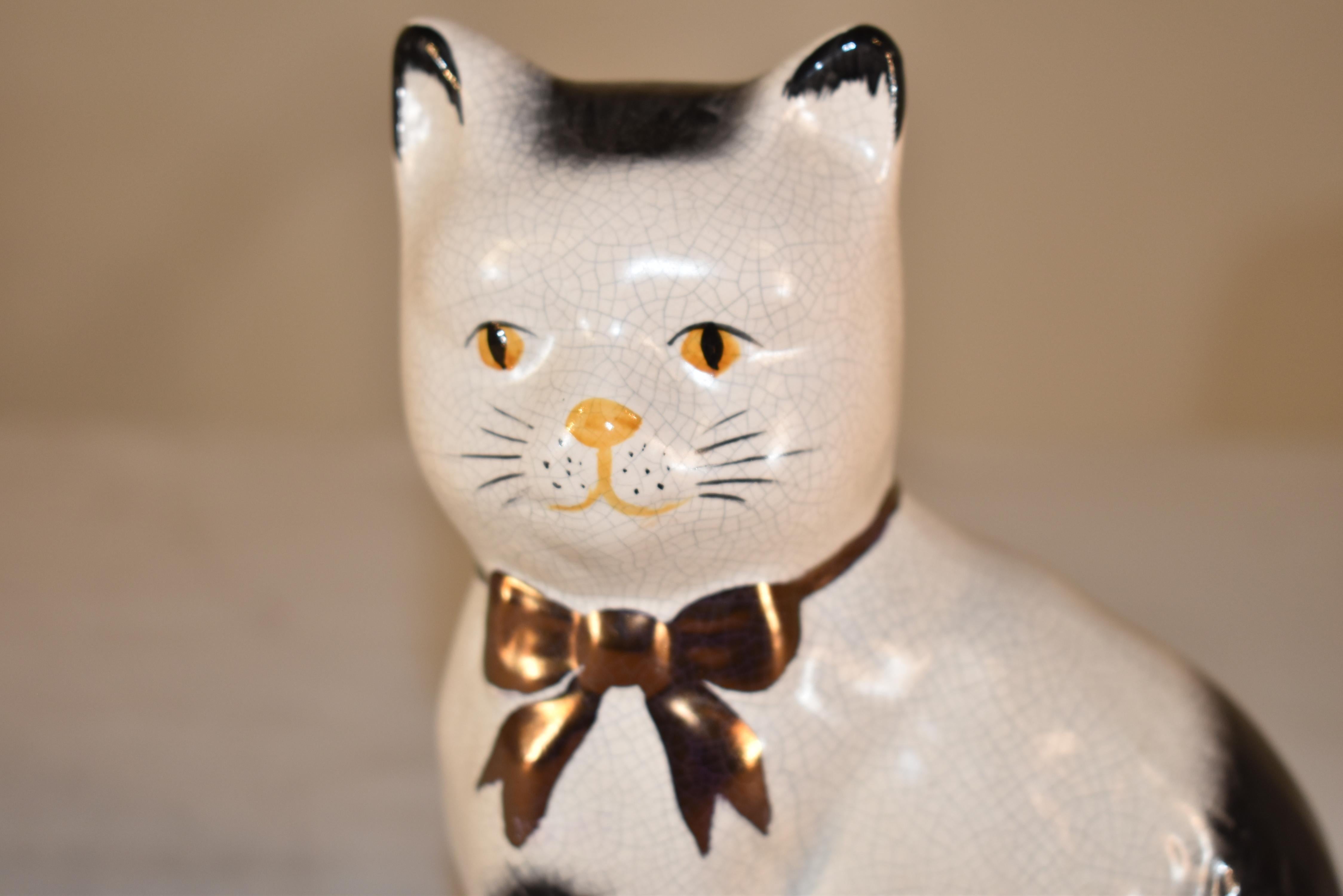 Circa 1970 vintage figure of a cat from the Staffordshire region of England.  The cat is decorated in black and white, and has a gold bow around its neck.  This is a nice model, as it has separated front legs.  
