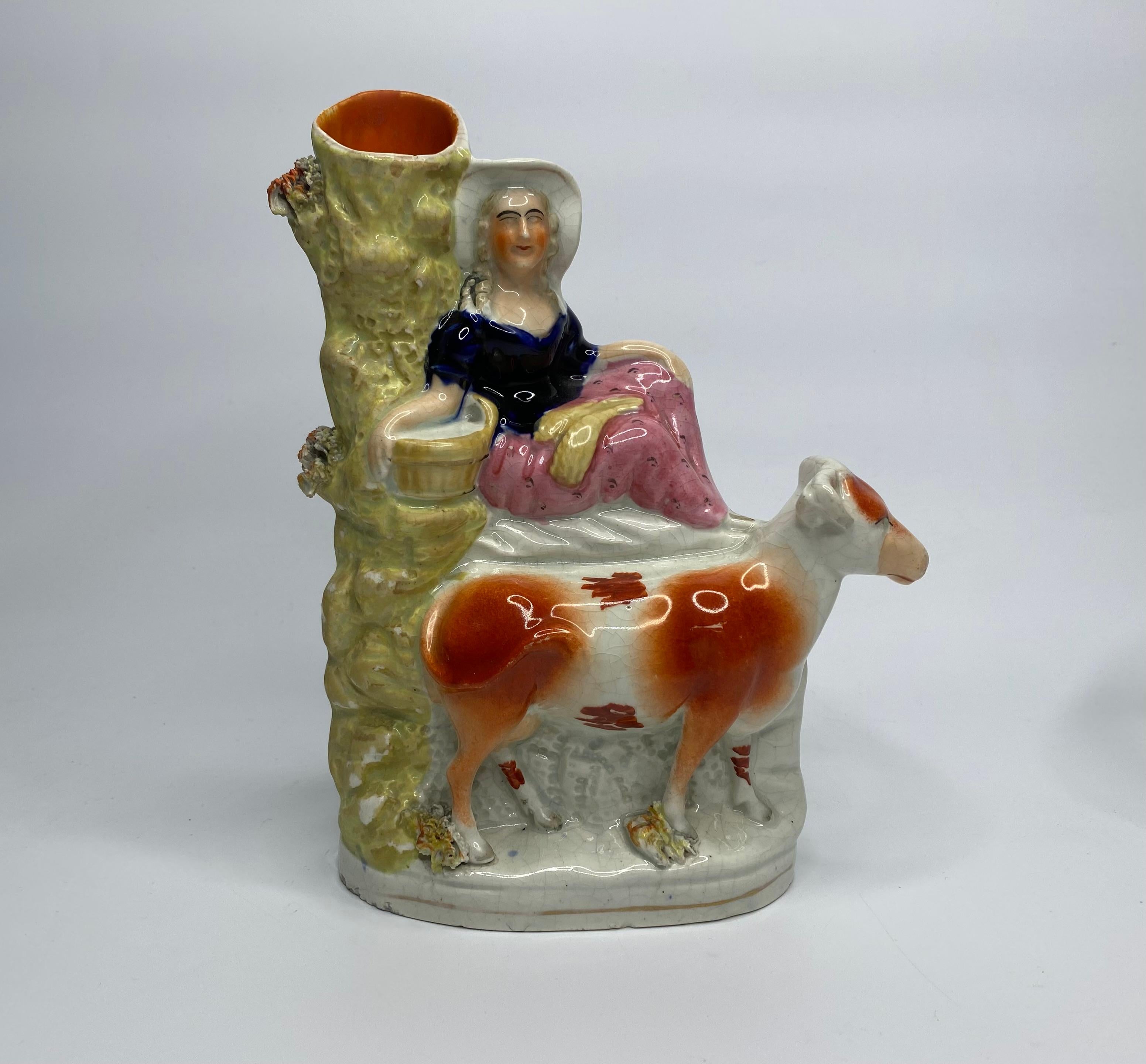 Pair of Staffordshire pottery spill vases, c. 1860. Modelled as a herdsman, and a milkmaid holding milk pails, sat upon rockwork, above their cows, before tree trunks, forming the spill vases.
Decorated in typical enamels, and having single gilt
