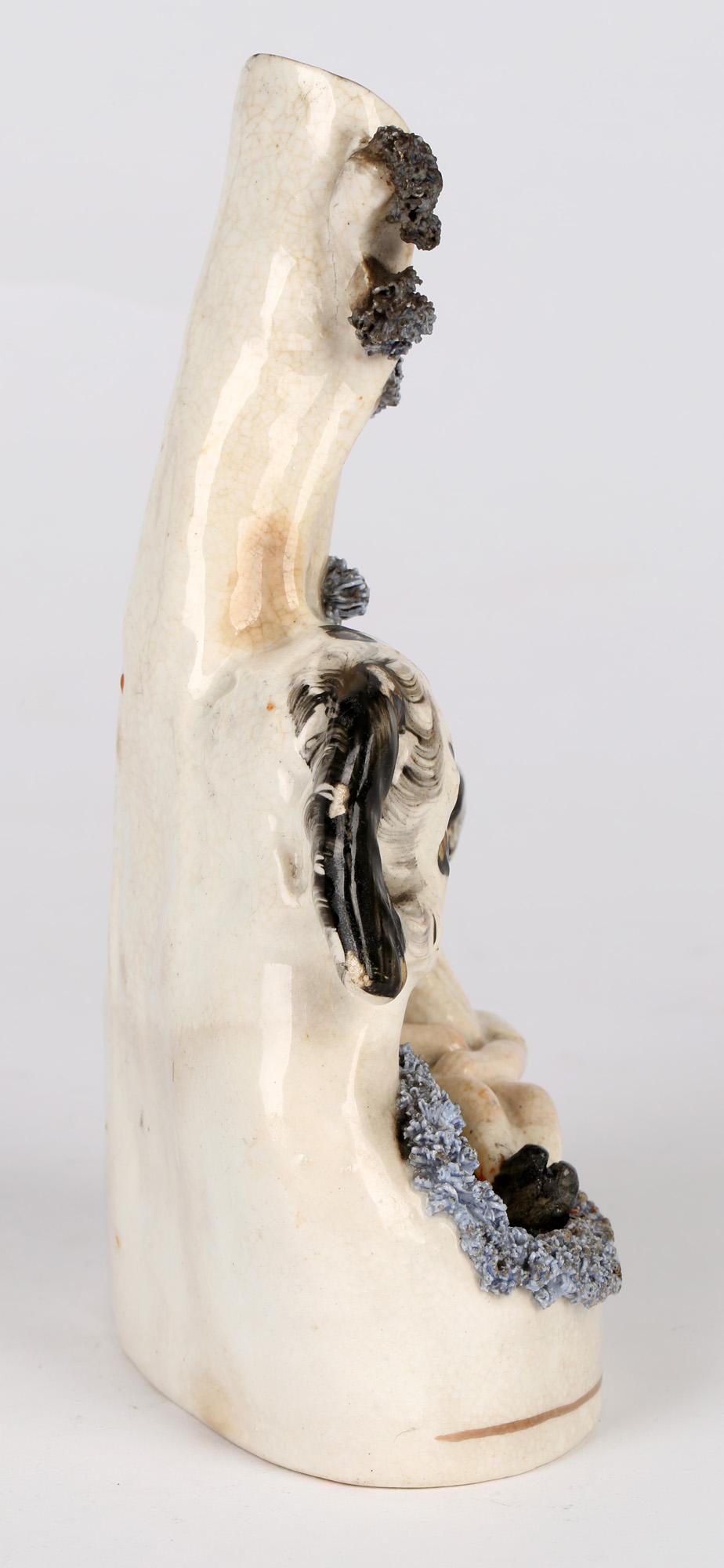 Raro e inusual jarrón antiguo inglés de Staffordshire con forma de perro que salva a un niño que se ahoga y que data de mediados del siglo XIX. El jarrón vertedor se alza sobre una base ovalada y representa a un gran perro que levanta a un niño de