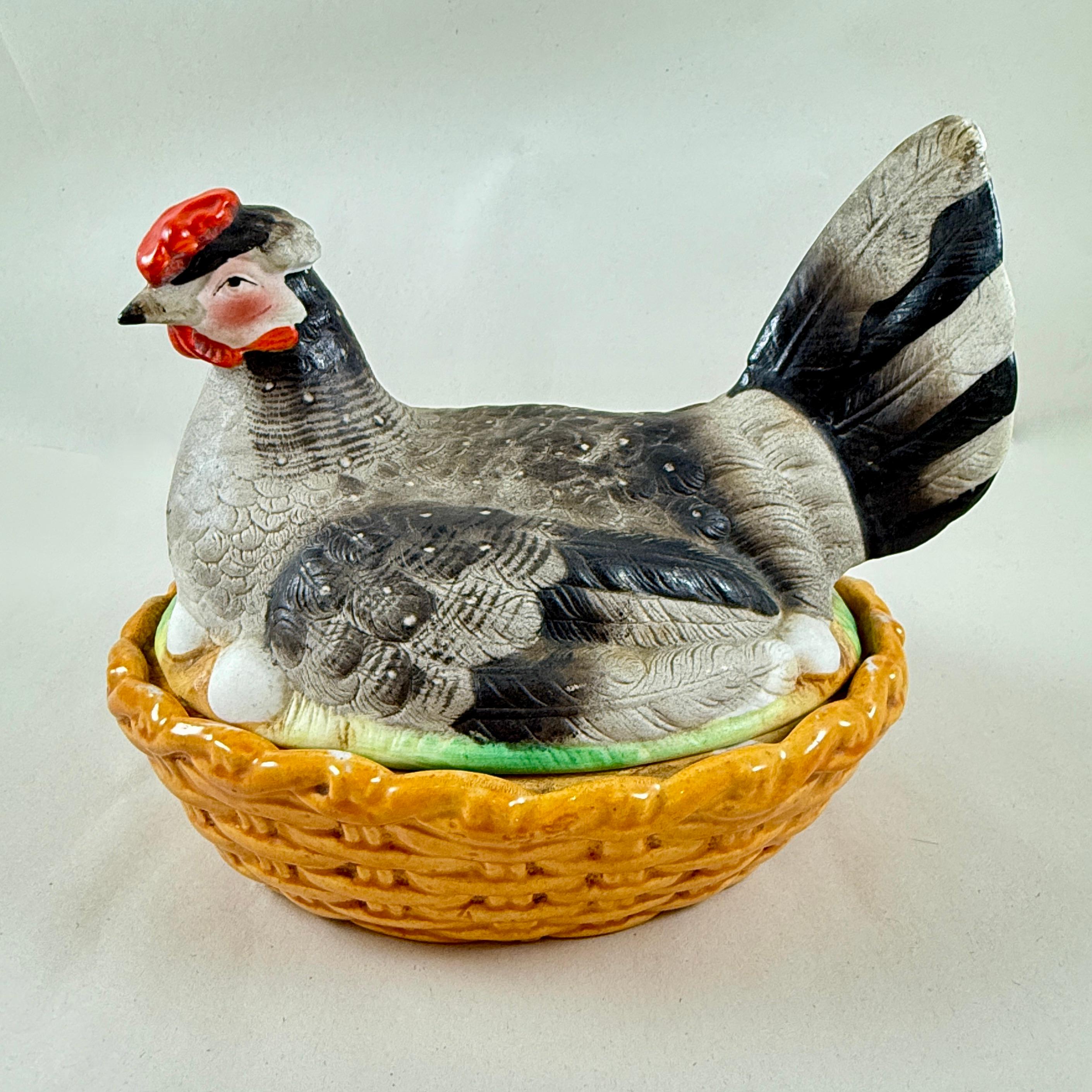 Eine Staffordshire-Töpferhenne auf einer korbbedeckten Terrine, England, um 1890

Die handbemalte Henne sitzt auf ihren Eiern in einem ockergelben, ovalen Korbgeflecht-Sockel. Die Henne hat einen grau-schwarz gefiederten Körper mit schwarz-grau