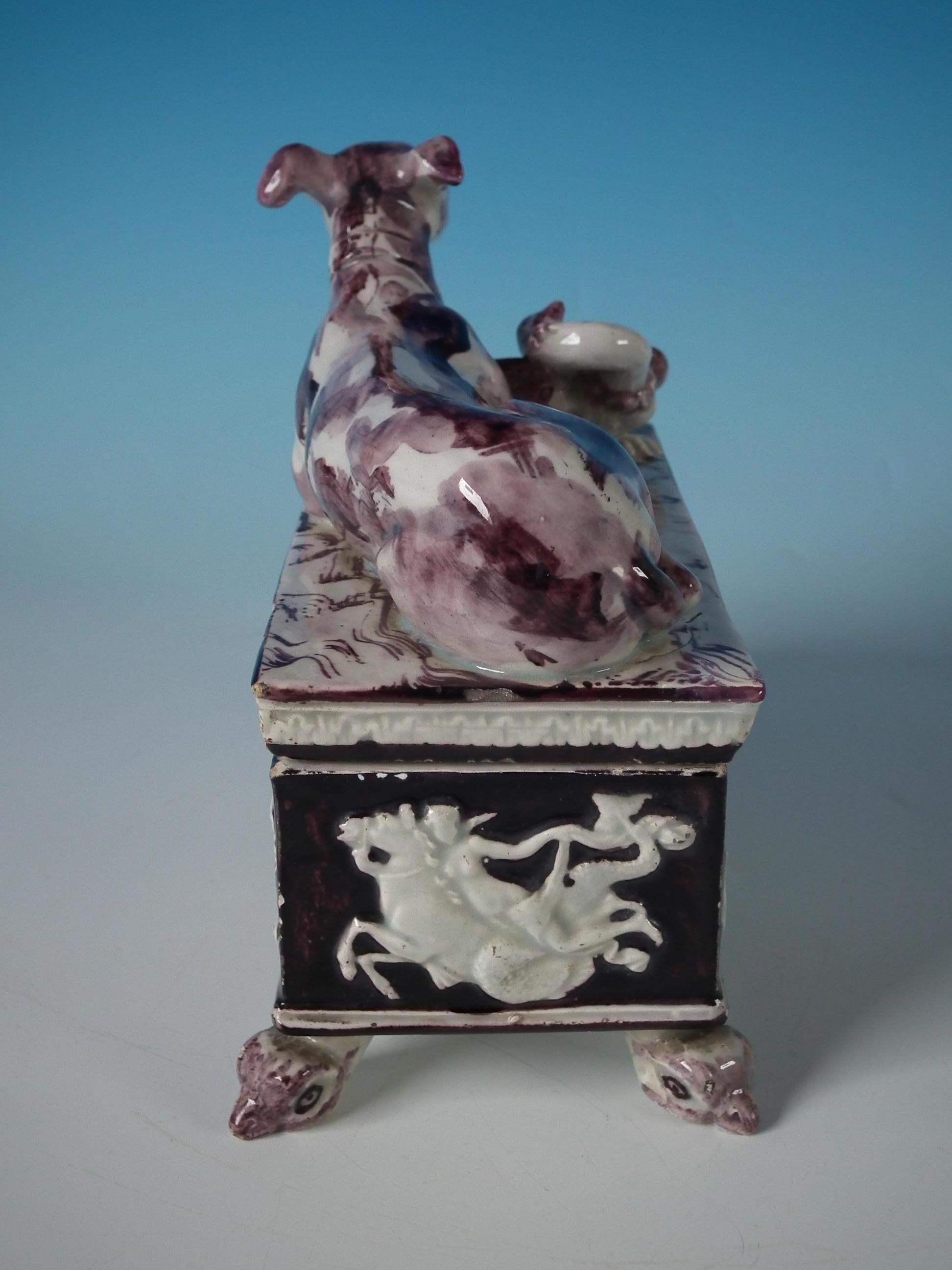 Staffordshire pottery Pearlware box and cover which features a recumbent greyhound and a bird to the cover. Pictorial scenes in relief to the sides of the box. The whole, stood on a footed base. Decorated 'in the round', decoration to front and