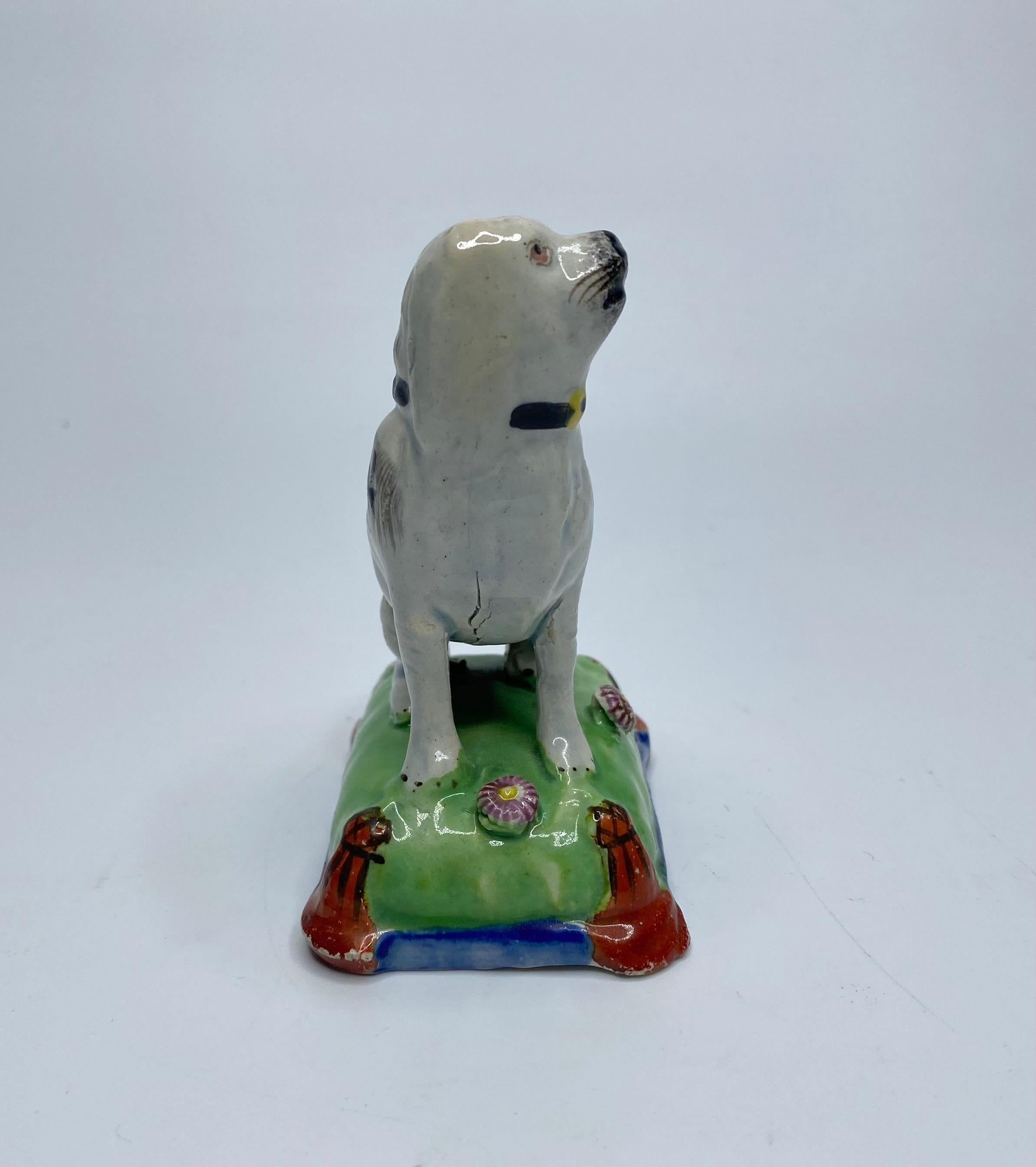 Chien assis en faïence perlée de la poterie du Staffordshire, C.I.C. Joli modèle, représentant un chien tacheté de noir, assis sur un coussin.
Le coussin émaillé vert et bleu, orné de deux têtes de fleurs et de glands rouge fer, noués aux coins.
Le