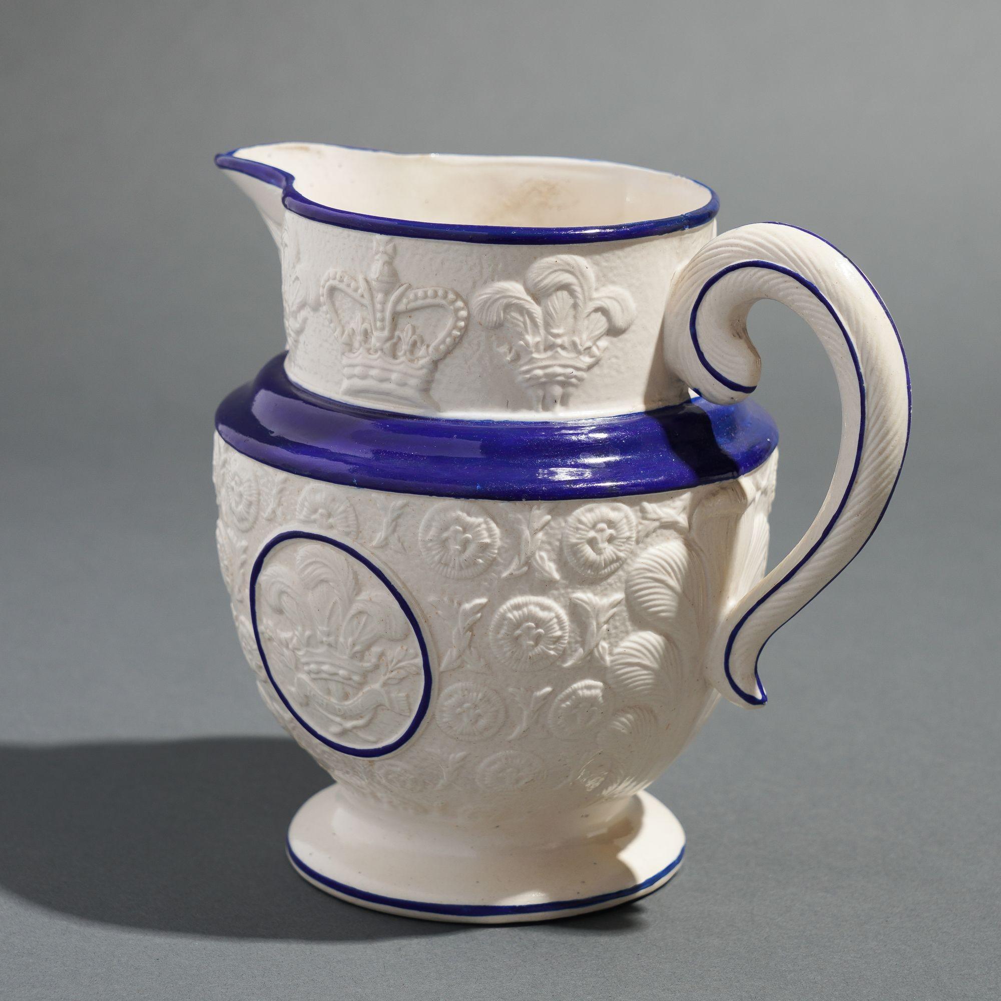 Commemorative Staffordshire pitcher celebrating the coronation of the Prince Regent as George IV. The pitcher has a patterned field surface decoration centering on a cobalt blue circle which encloses a design of the Prince of Wales feathers, which