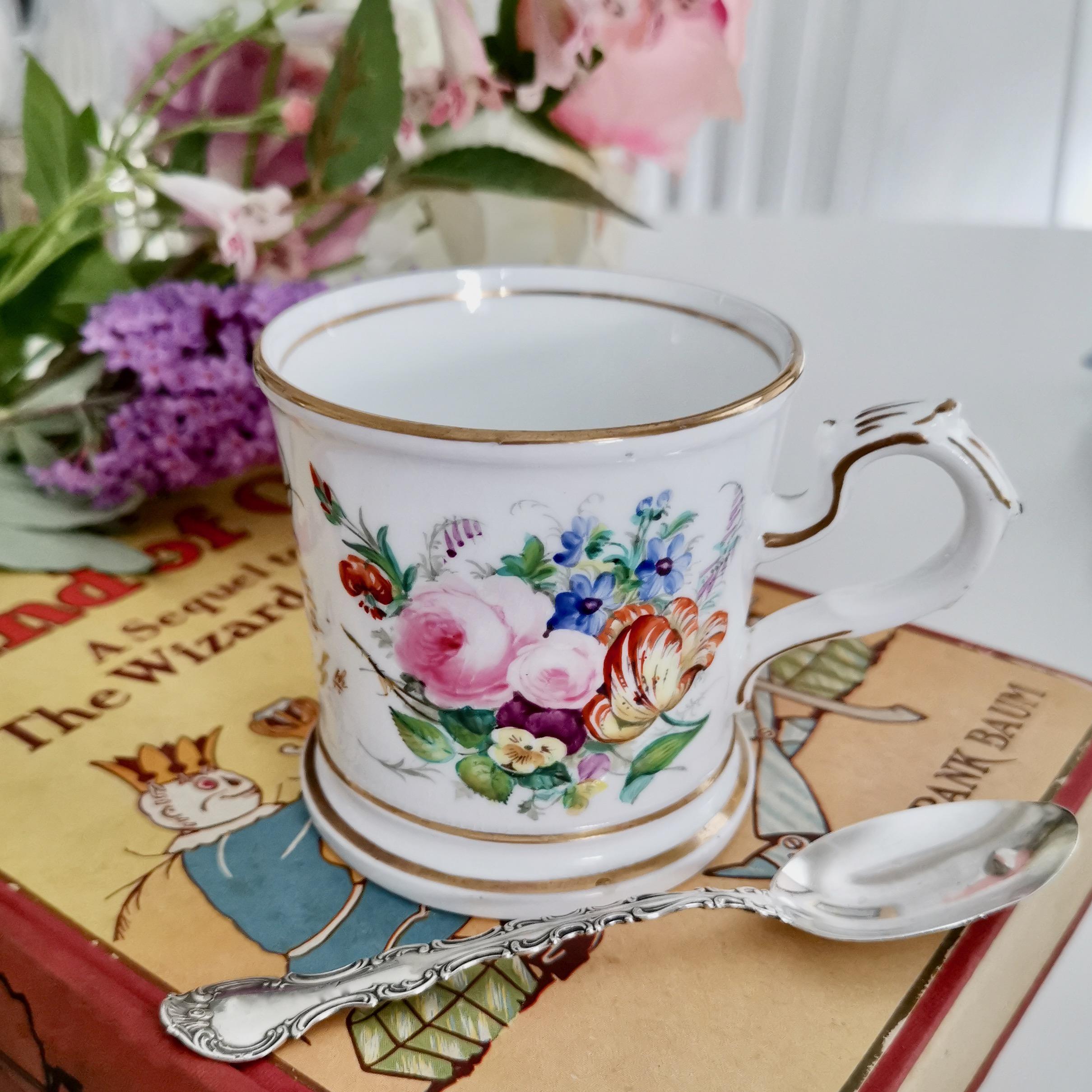 This is a beautiful porcelain christening mug made in Staffordshire in the year 1867, which was the Victorian era. The mug has hand painted flowers on a white ground, and the gilded text 