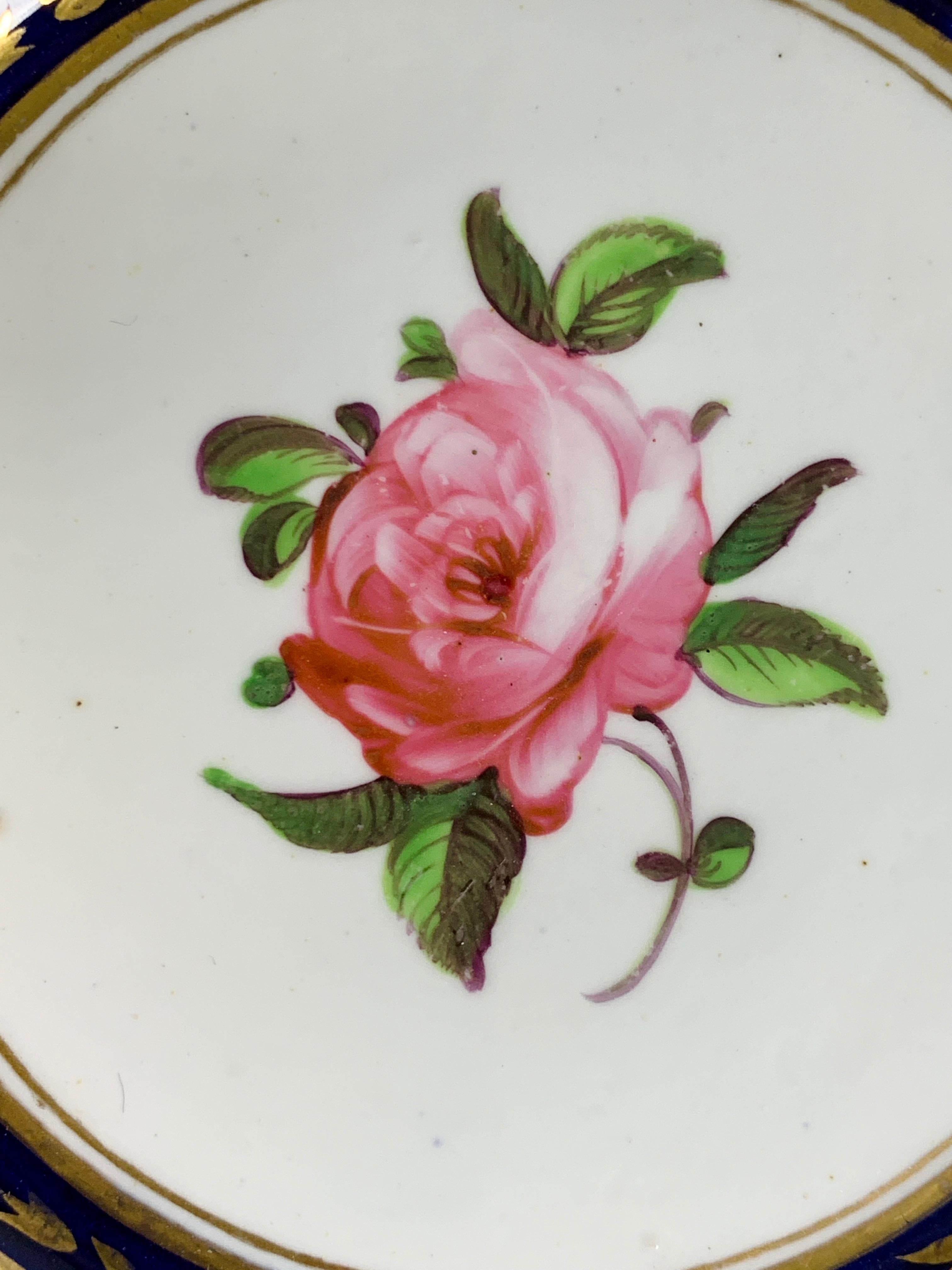 A delightful English porcelain dish made circa 1820 hand-painted with exquisite flowers on crisp white porcelain.
In the center is a lovely pink rose. Other roses, forget me nots, and other flowers with trailing vines surround it, all bursting with