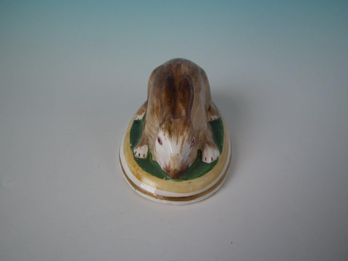 Figurine en poterie de Staffordshire représentant un lapin, couché sur une base ovale. Embellissement doré terne. Décoré 
