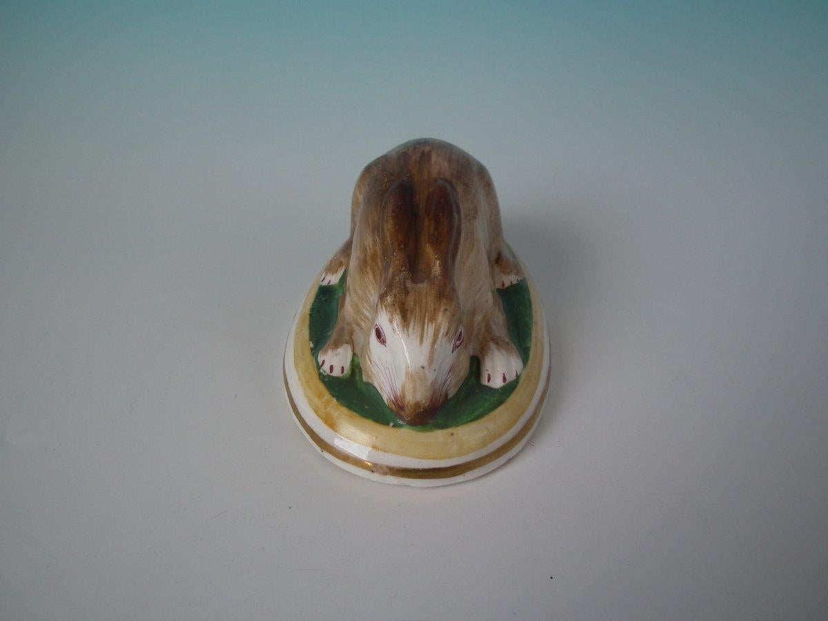 Figura in ceramica Staffordshire che raffigura un coniglio, sdraiato su una base ovale. Abbellimenti dorati opachi. Decorato 