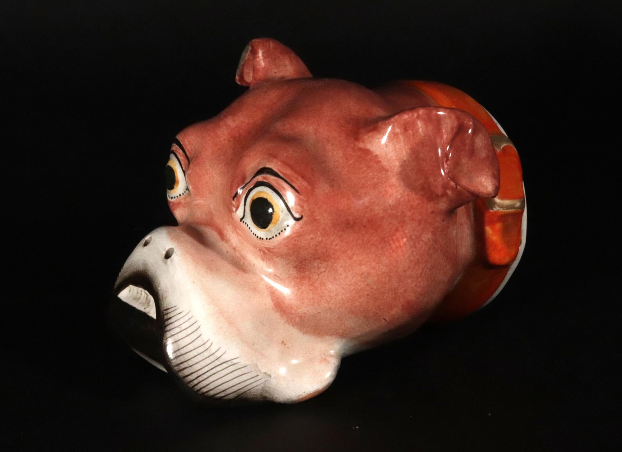 Staffordshire Bulldog Stirrup Cup,
Circa 1820

The pearlware pottery stirrup cup is modeled in the form of a bulldog head and sports an orange collar with a gilt buckle.   The dog has ears curling over and is painted in a naturalistic brown color. 