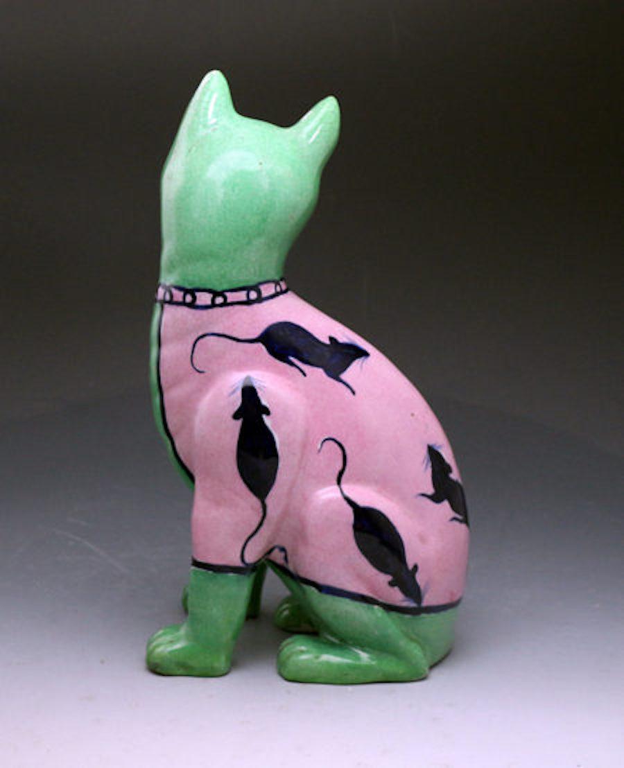 Dated: 1900 Staffordshire, England

This comical English pottery figure of a green-colored seated cat inspired by a model made initially by Emile Galle of Nancy France. The cat is wearing a rose pink waistcoat which is decorated with seven blue