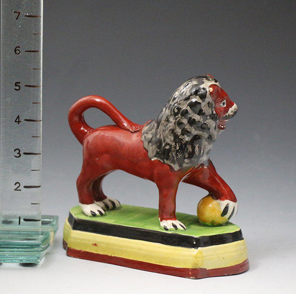 Antique Staffordshire pottery figure of a lion on a base with paw on ball early 19th century. The figure is well colored with a good pearlware glaze and dates to the early 19th century, England.