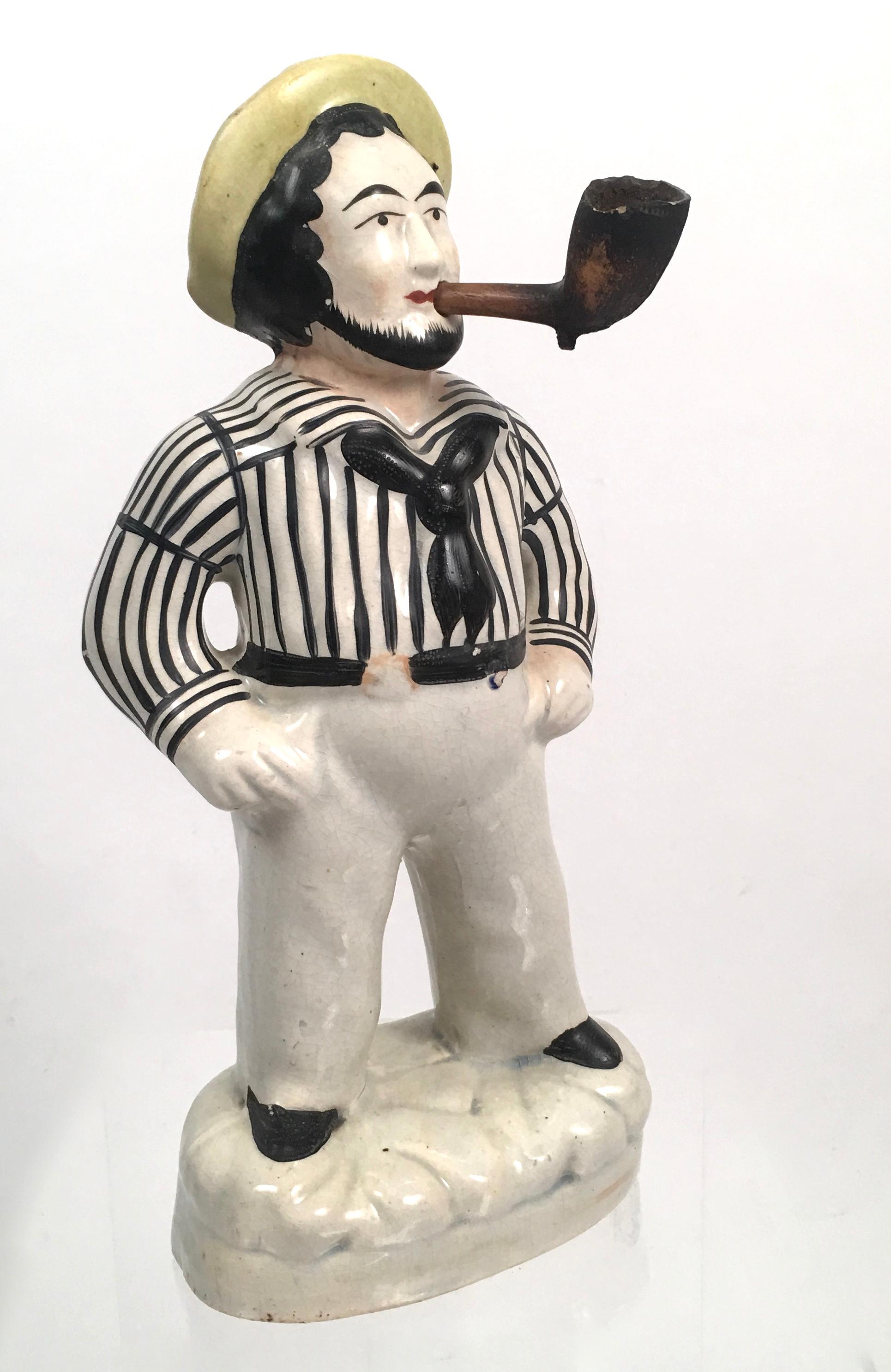 A hand-painted Staffordshire pottery figure of a sailor, English, circa 1840, commonly referred to as Jack Tar, depicting a bearded sailor wearing a yellow cap and traditional blue and white striped shirt, navy blue scarf, white pants with black