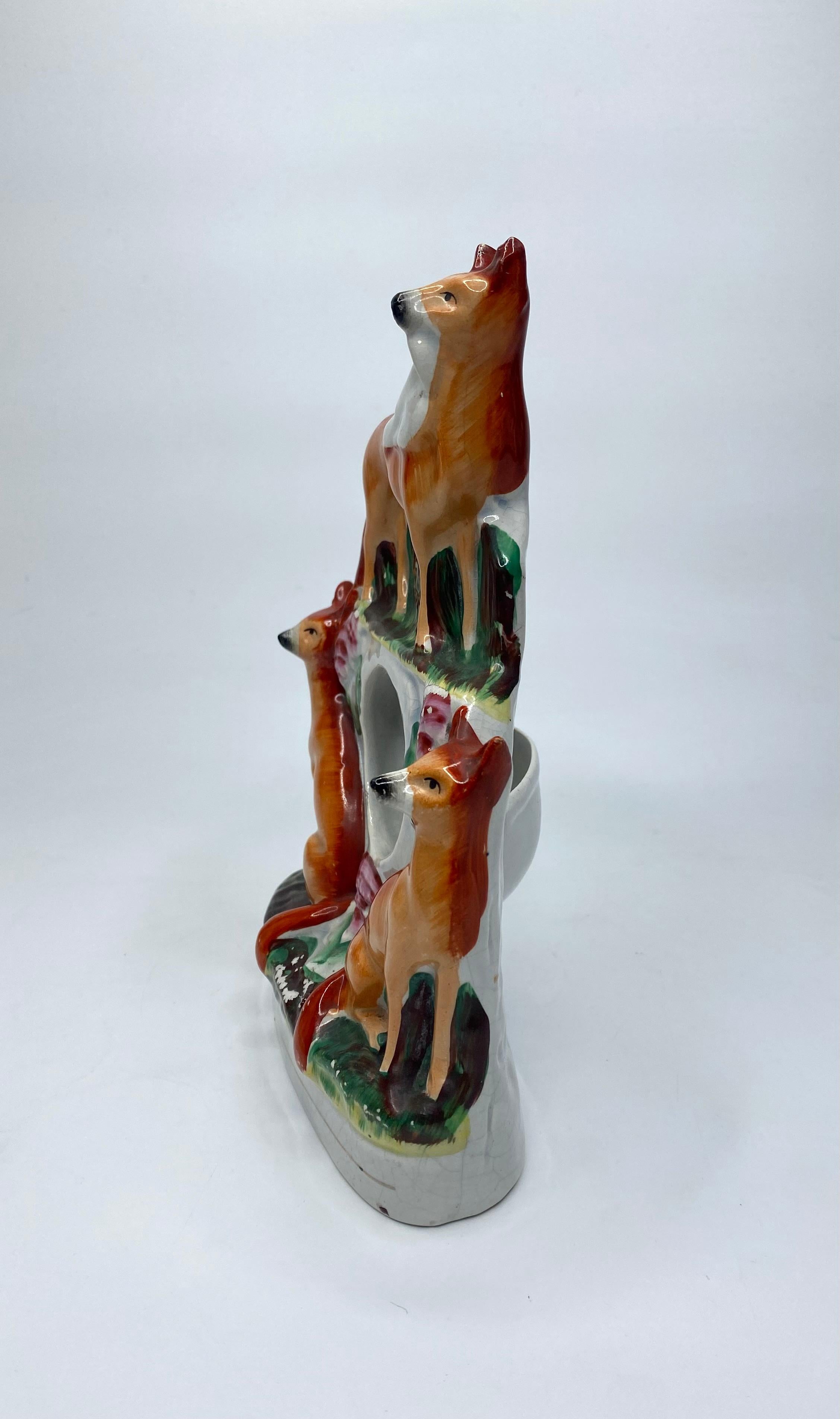Staffordshire pottery watch holder, c. 1860. Modelled as two foxes, seated either side of the watch holder, with a further fox, with its catch, stood above the watch holder.
Coloured in naturalistic enamels, with a single gilt line to the oval