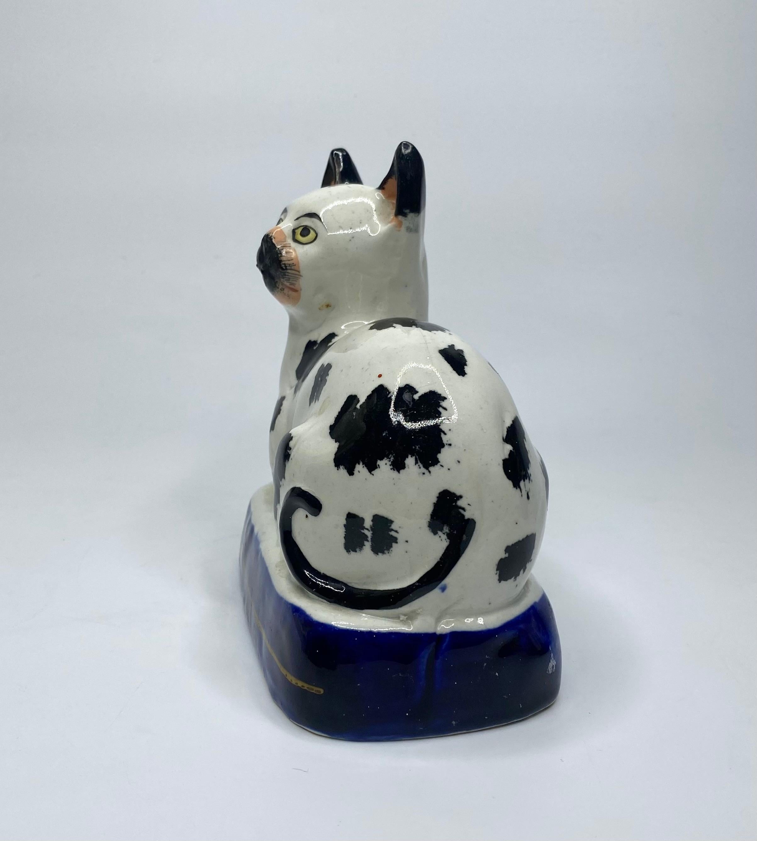 Rare and fine Staffordshire pottery cat, c. 1850. The recumbent cat, painted with large underglaze black spots, and having yellow eyes. Set upon an underglaze cobalt blue base, with a single gilt line.
Factory crazing, and firing faults. No damage.