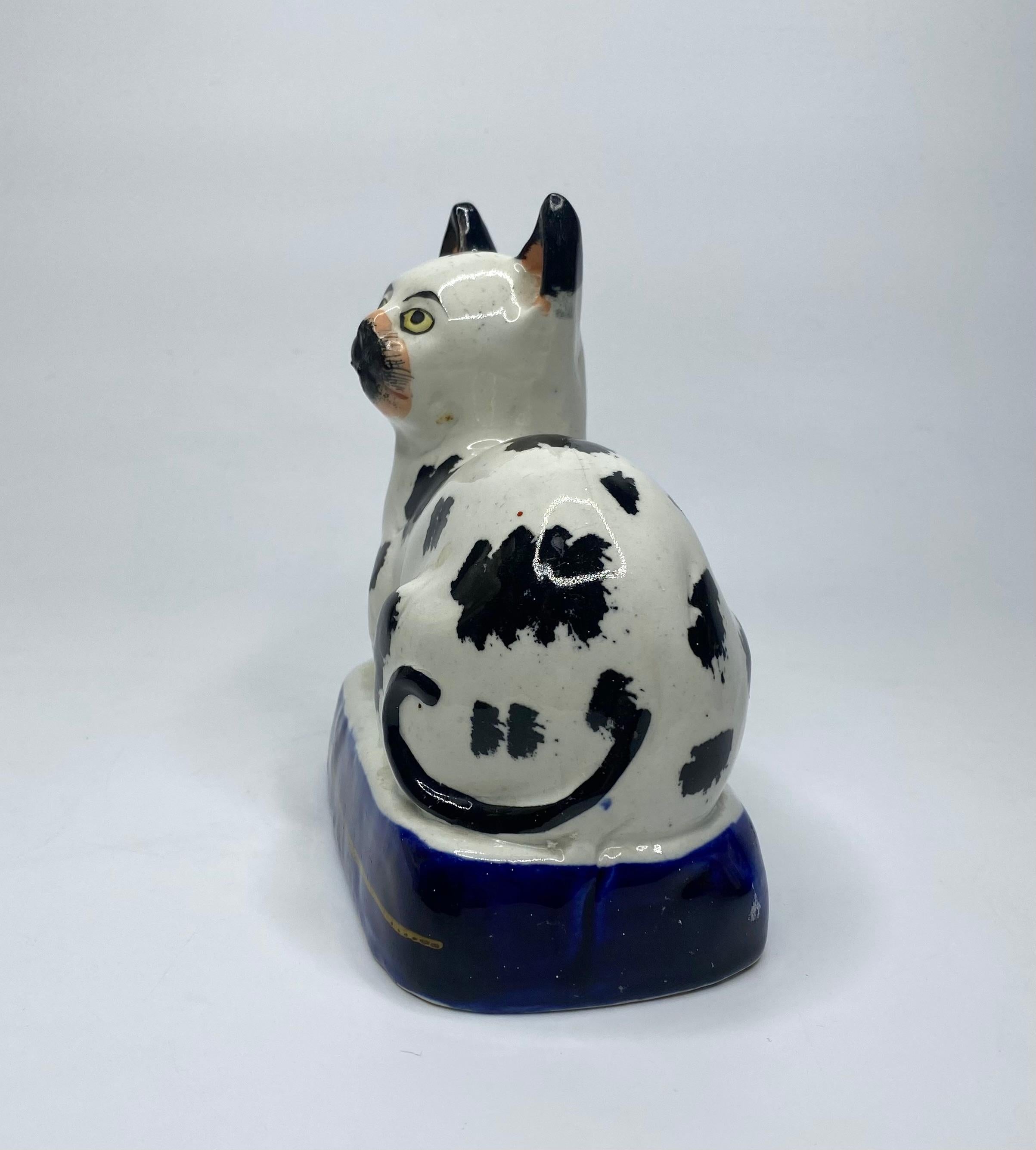 Rare et beau chat en poterie du Staffordshire, C.I.C., vers 1850. Le chat couché, peint avec de grandes taches noires sous glaçure et des yeux jaunes. Sur une base bleu cobalt sous glaçure, avec une seule ligne dorée.
Craquelures d'usine et défauts