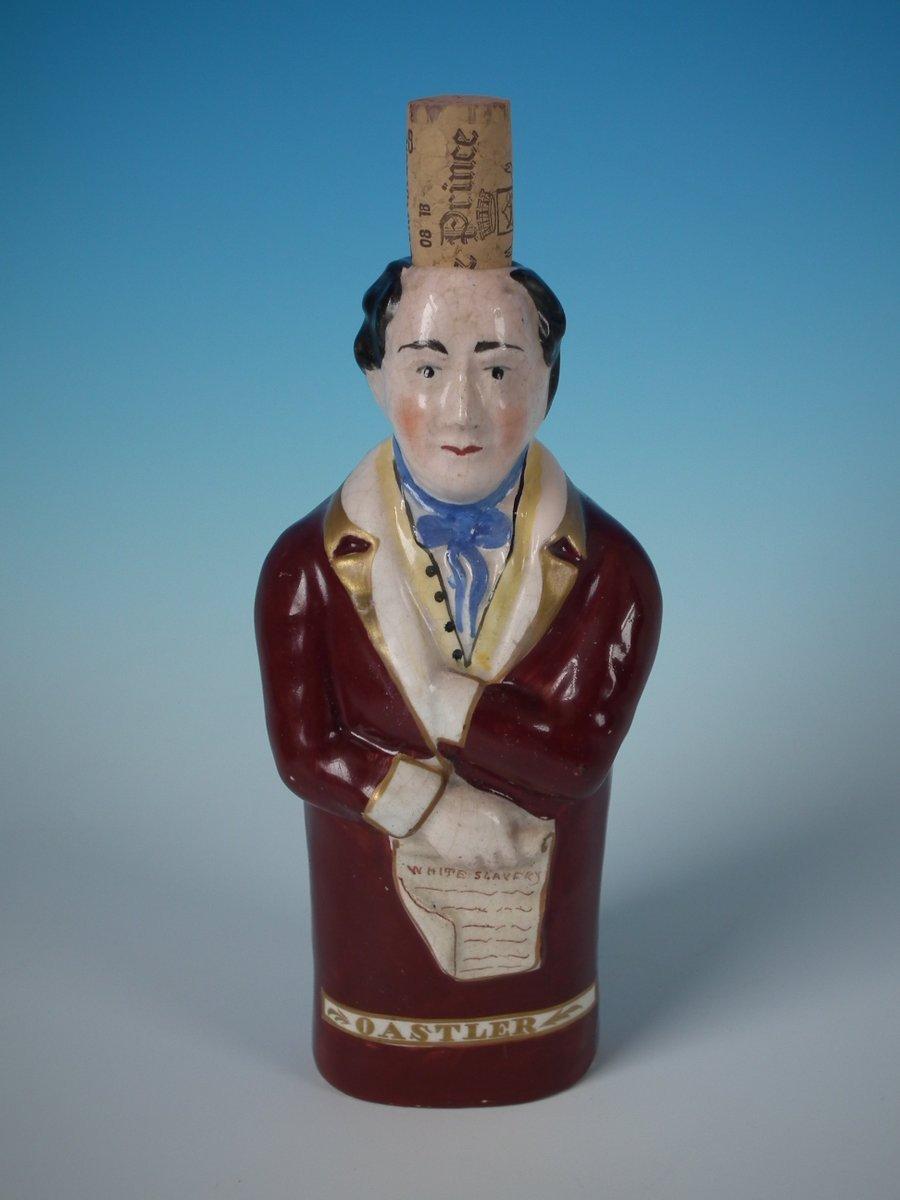 Staffordshire Pottery bottle/flask with a political theme which features a man holding a scroll entitled, 'WHITE SLAVERY', stood directly on the ground, no base. The piece is titled, 'OASTLER' . Dull gilt embellishment. Decorated 'in the round' -