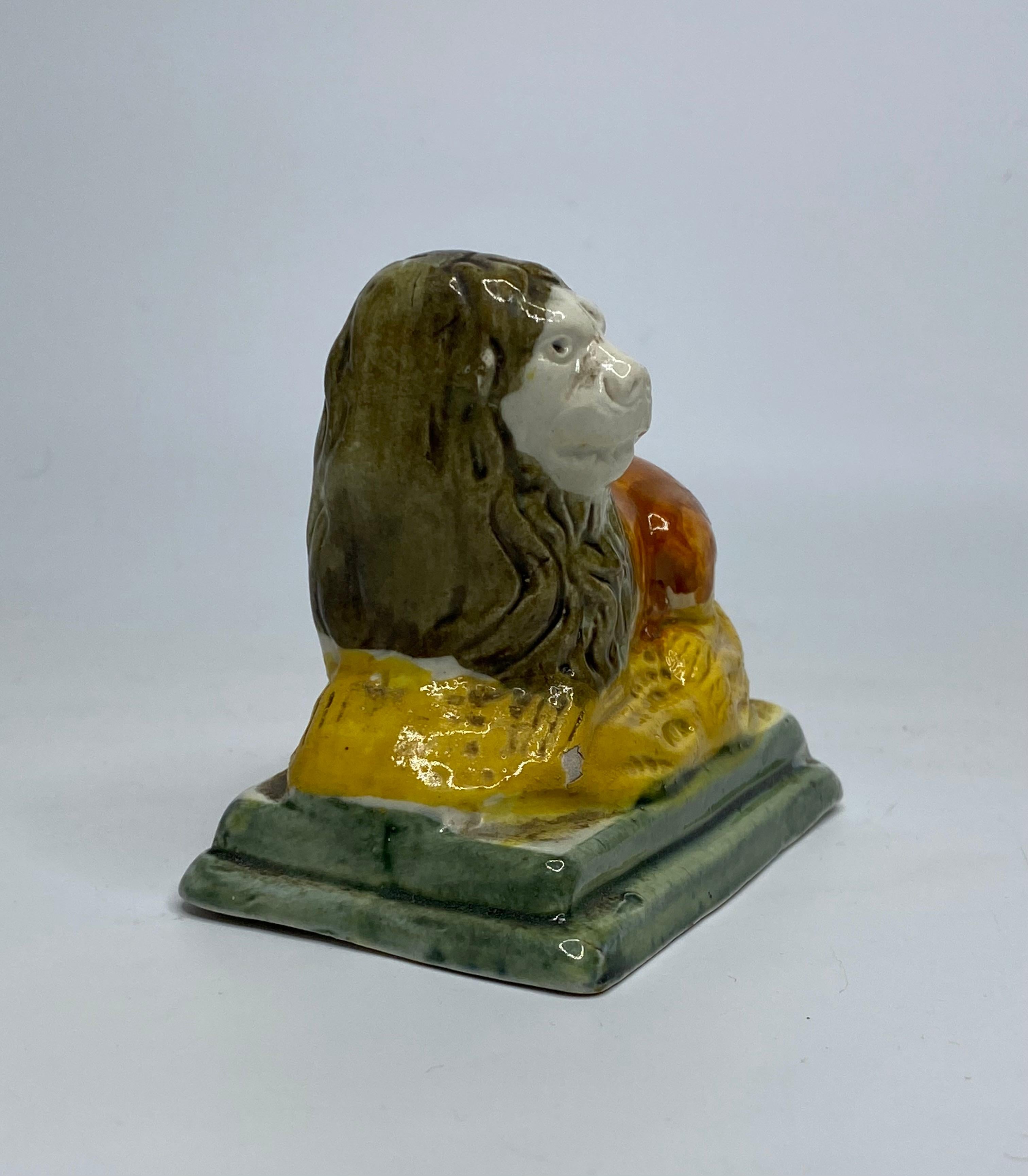 Staffordshire pottery figure of a lion, c. 1790. The recumbent lion, covered in Pratt type glazes, laid upon a yellow mound base. Set upon a green glazed stepped pedestal base.
Having a hollow base.
Length – 9 cm, 3 1/2”.
Height – 8 cm, 3