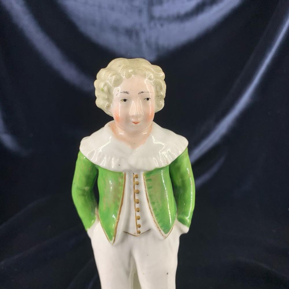Staffordshire 'Schoolboy' figure, modelled standing with hands in pocket, smartly dressed in a green jacket over white breeches with gilt cuffs, on a circular plinth with green band. 
Unmarked, unknown Staffordshire maker, 
circa 1830.


Ref.