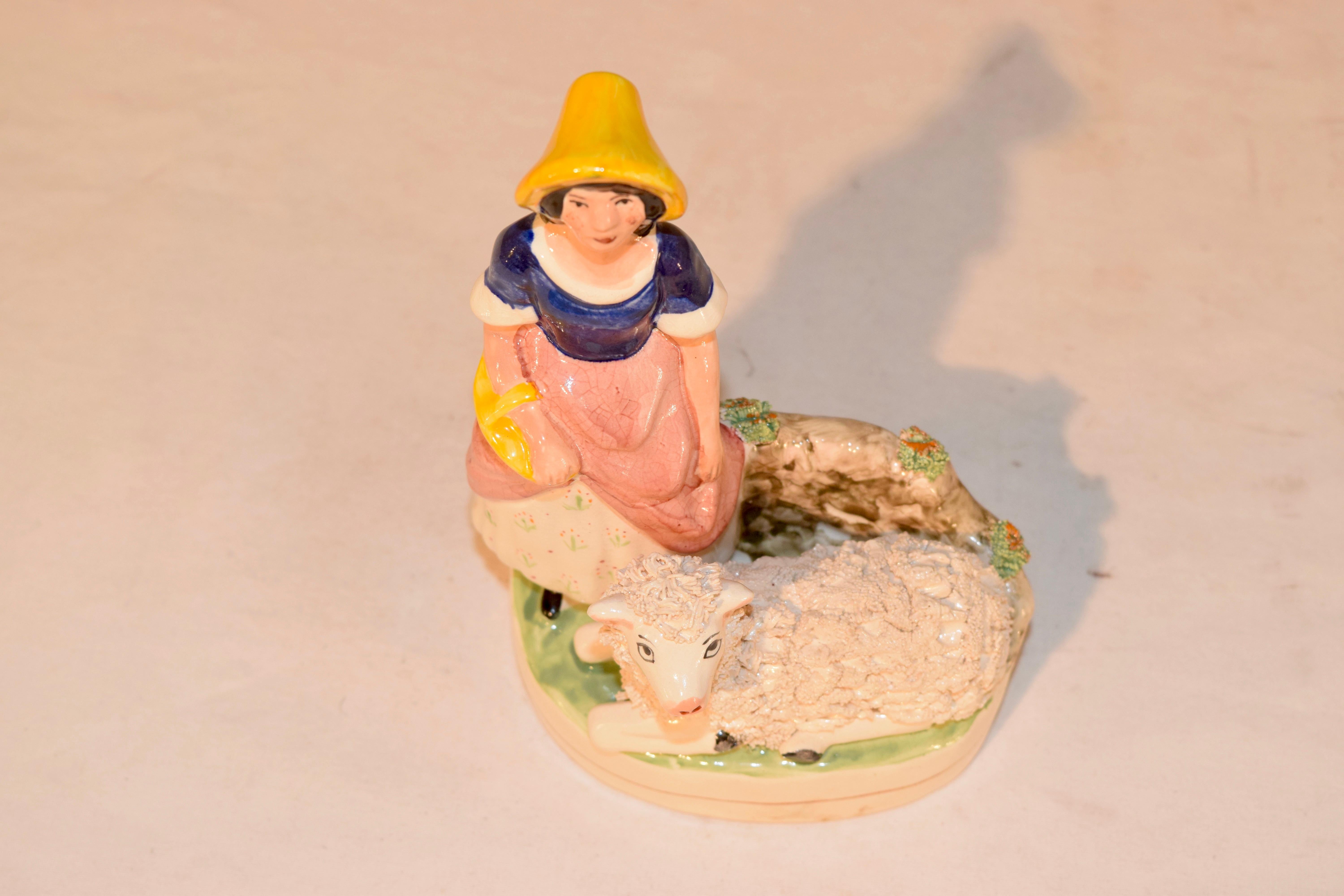 Wonderful hand made Staffordshire figurine from England of a lady and a lamb. The lamb is lying in front on the grass with the lady behind him with what appears to be a basket on her arm and a yellow hat. Lovely form.