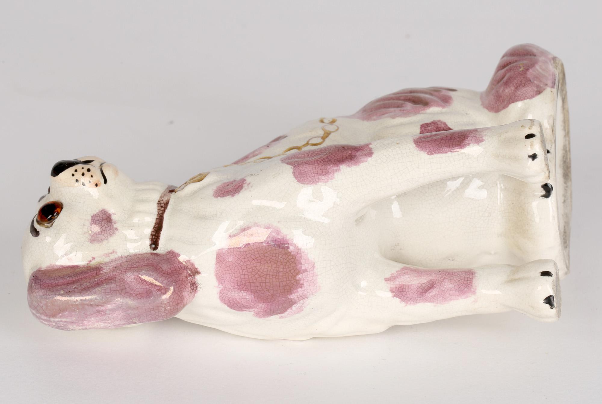 Unusual Staffordshire pottery dog modelled seated and facing decorated with pink lustre patches and applied with glass eyes with collar with gold lock and chain dating from around 1880. The dog has well painted features and is not marked.

See