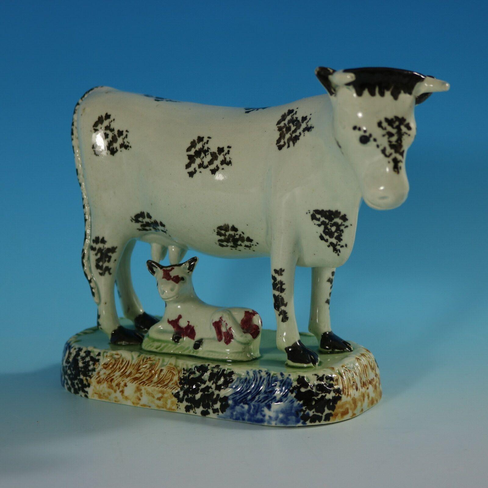 Staffordshire Yorkshire Pottery Prattware figure which features a cow with a recumbent calf, stood on a rectangular base, with grassy detail. Speckled blue, orange and black around the base.