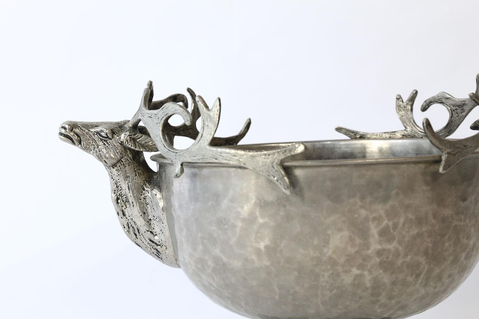 This beautiful hammered metal footed bowl is embellished with stag heads and a textured base. The base resembles roots of a tree for a woodland effect. This piece could be used as a centerpiece with flowers or as an ice bucket to chill wine or