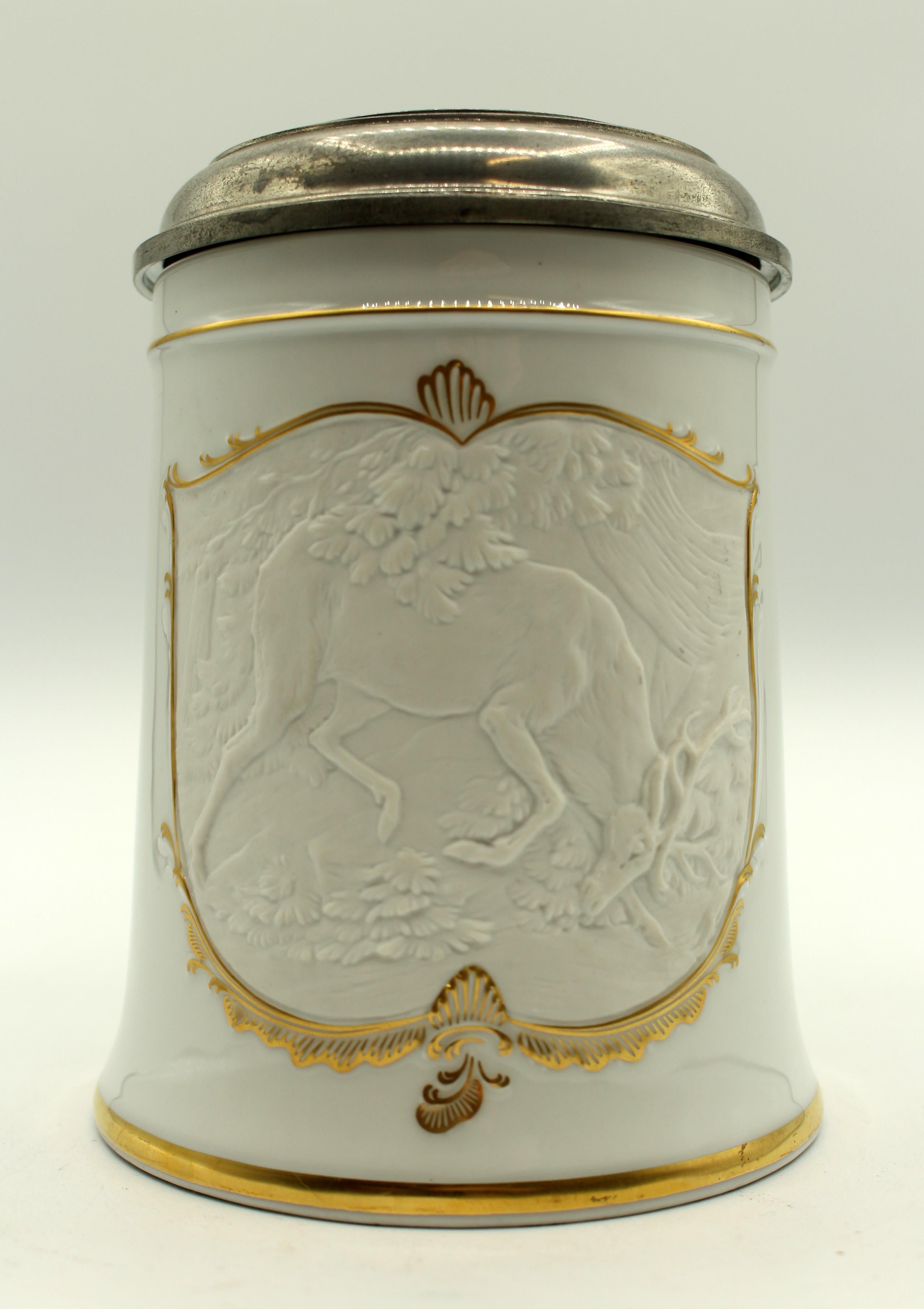1949-1990 Kaiser porcelain stein. W. Germany mark. Stag motif pewter top after the work of Johann Ridinger, a bisque bas relief of charging stag in rococo shield. Pewter flip top repeats stag motif. Measures:  4 3 / 8