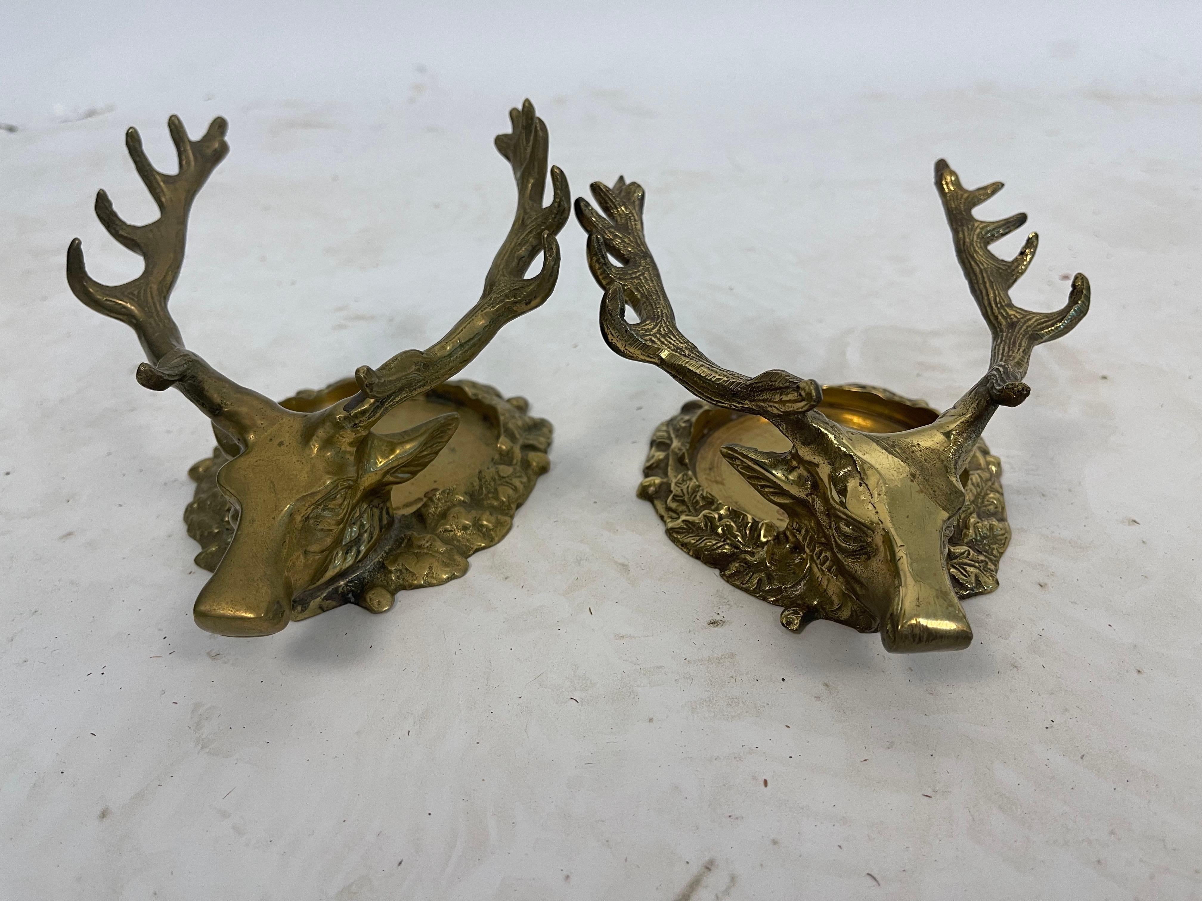 A near pair of brass wine bottle holders to protect your table from wine spills. Made of polished brass and formed into Stag heads with majestic antlers, these wine bottle holders would elevate any table setting. The stags have a decorative collar