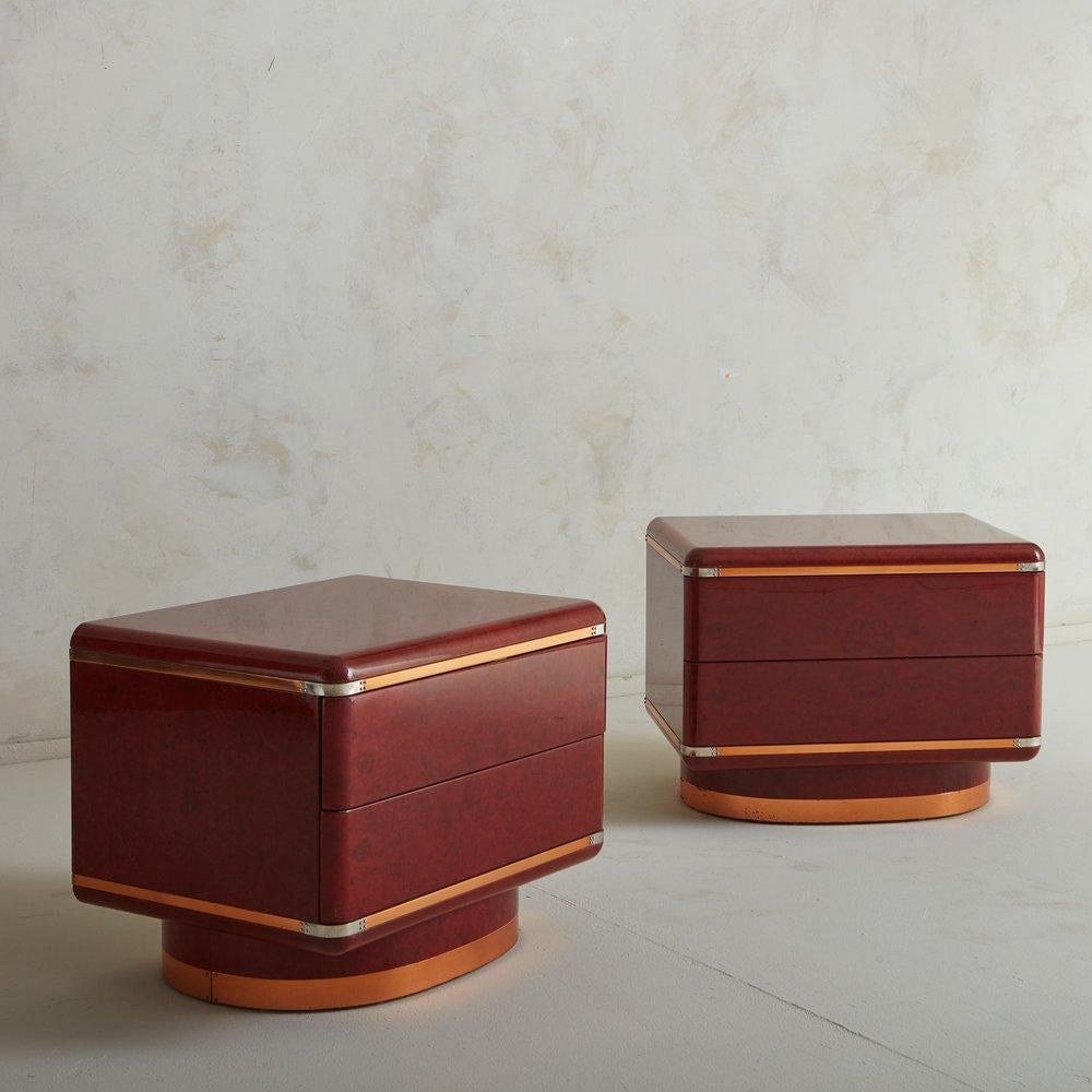 A pair of 1970s Italian nightstands in the style of Saporiti. These nightstands feature a red stained lacquered burl wood veneer with copper-tone metal + chrome detailing. They have subtly curved edges and two large drawers, offering significant