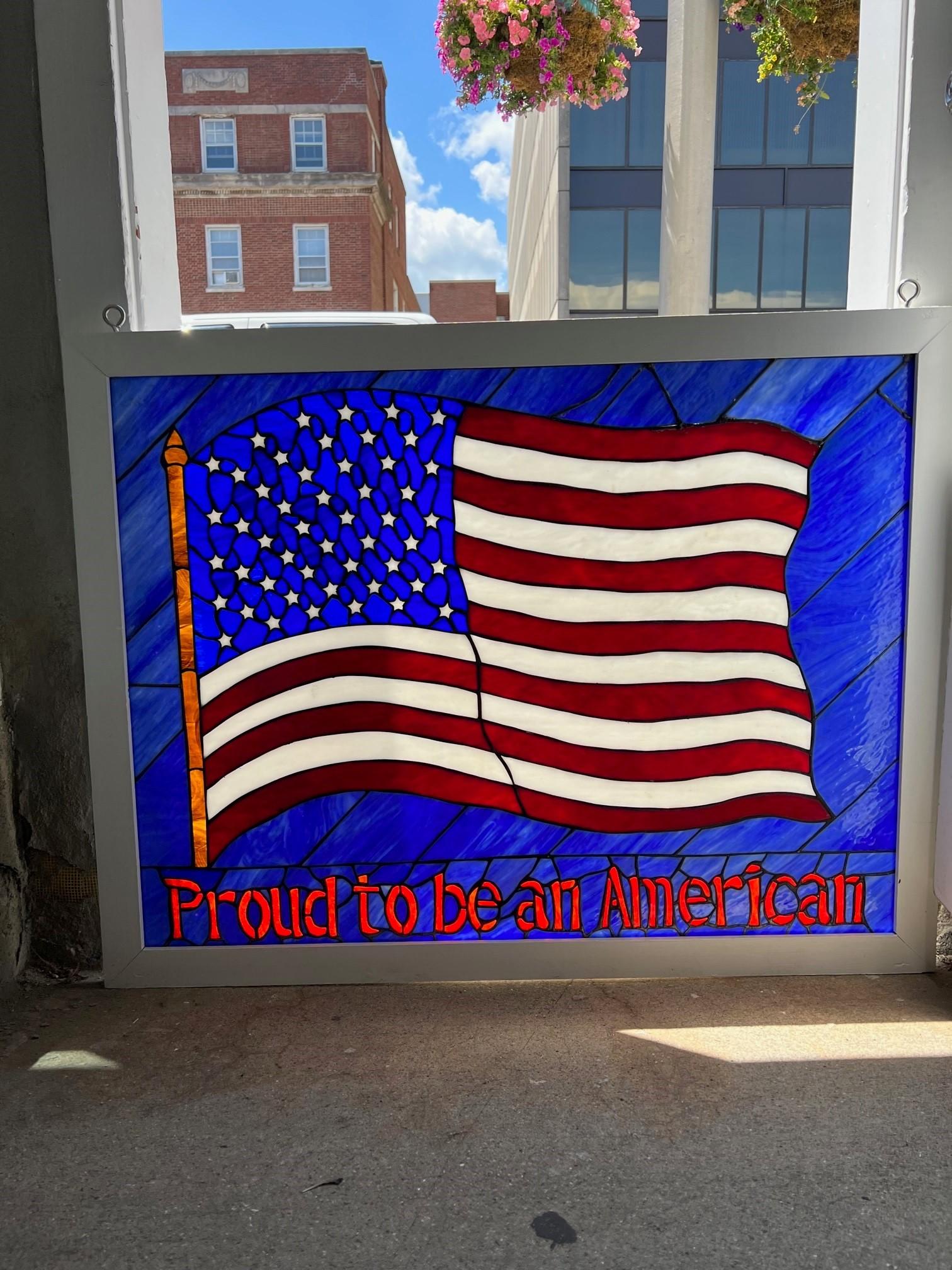 Beautiful stained glass window of an American flag with Proud to be an American in a wood frame painted white. This is not an old window it was made in 2001 after 911 to show support for the United States. Its in great condition no breaks and is