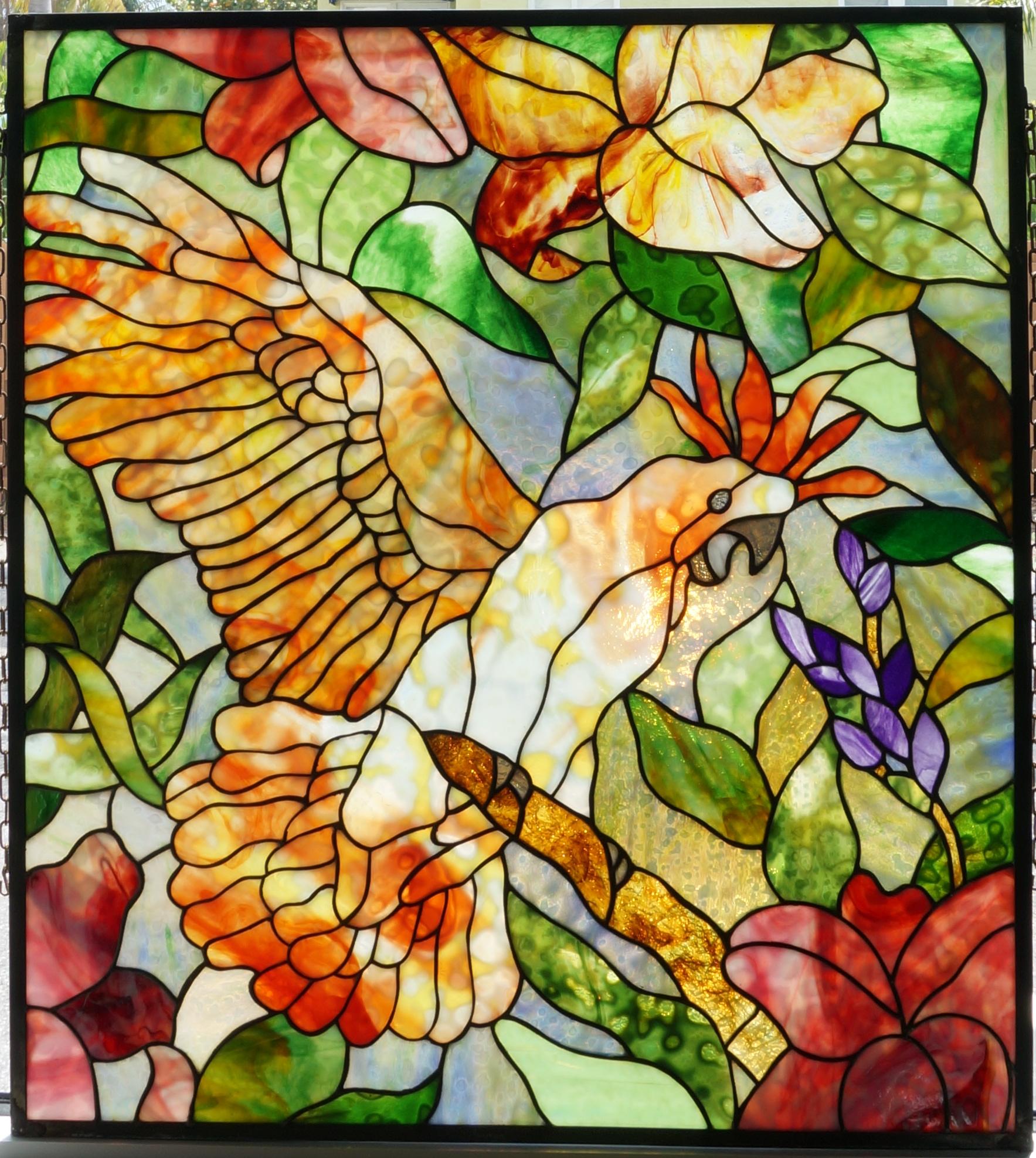 This stylish, dramatic and coloful stained glass panel was created by an artist only known as Abraham. The piece catches the cockatoo in a background of colorful tropical foliage. 

Note: There are two attached pieces of chain on either side of