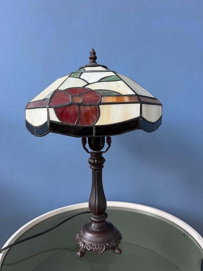 Lampe de bureau de style Tiffany avec un magnifique abat-jour en verre teinté. La base est en métal et l'abat-jour est en acrylique. Le vitrail produit un effet de lumière chaude. L'abat-jour peut être retiré de la base et positionné de la manière