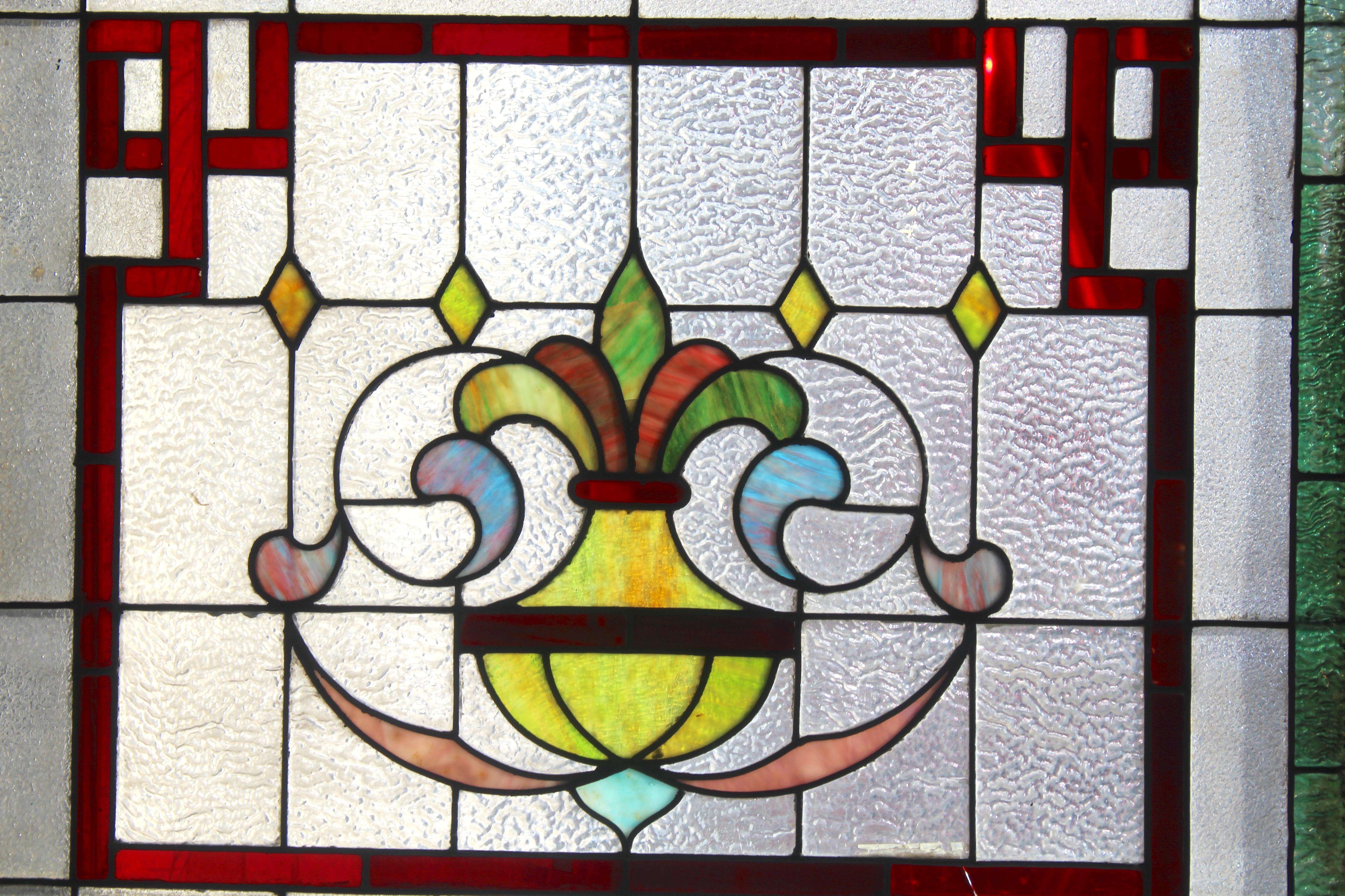 Esta vibrante vidriera procede de una granja de Pensilvania, y aún conserva su hermoso colorido. El borde está ribeteado dos veces en verde y rojo intenso, con cristal transparente texturizado y una pieza central estilo flor de lis. 
Las dimensiones