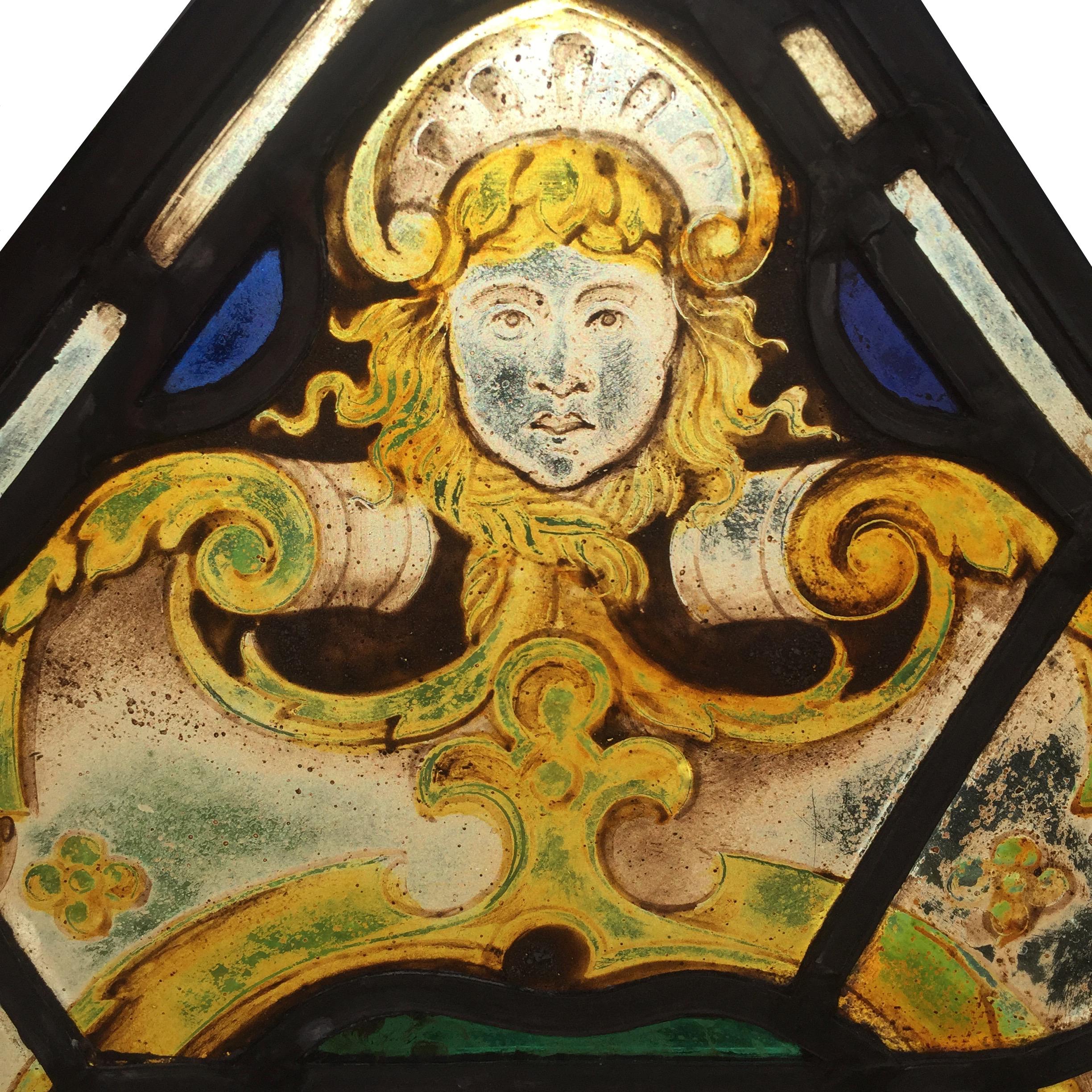 A very decorative section of hand-painted English stained glass, depicting a face and three wheatsheafs. 

The lower section of the panel reads 